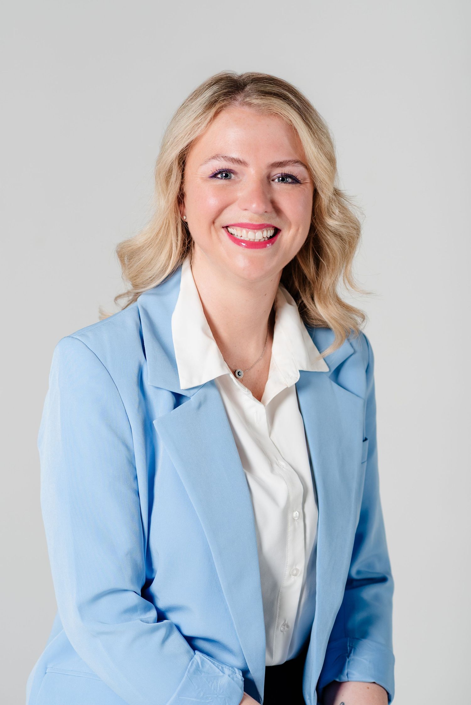 Woman smiles for headshot, wearing a light blur blazer