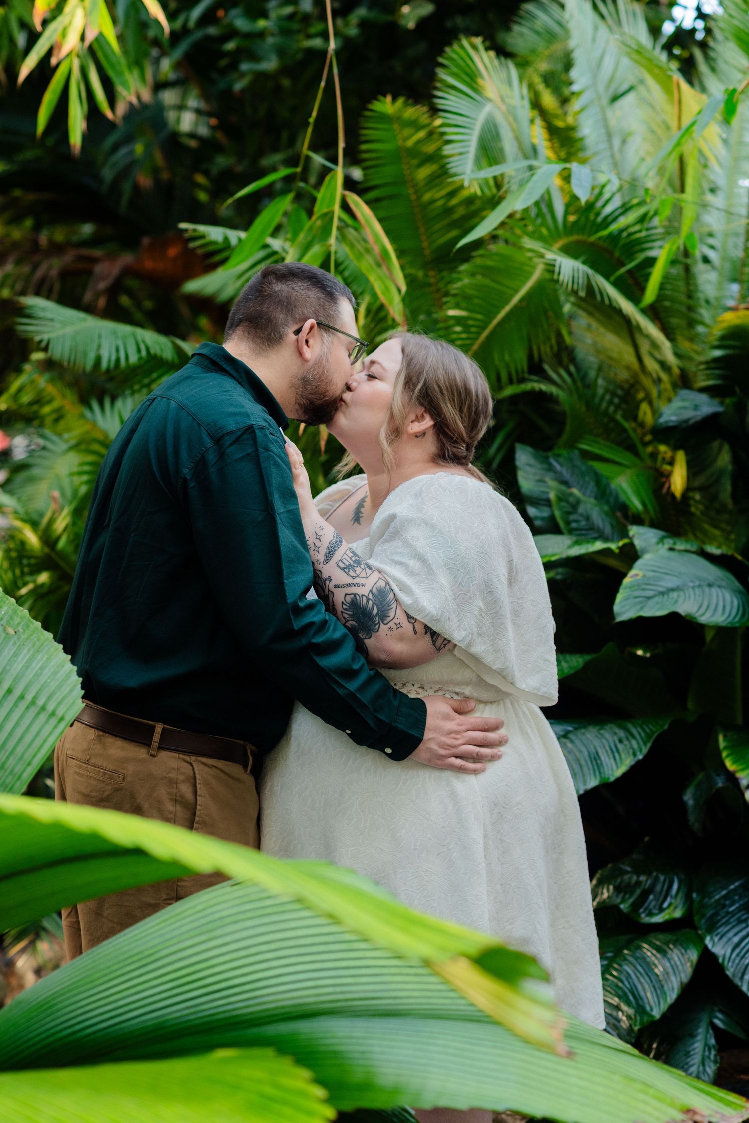 man and woman kiss in leafy greenhouse