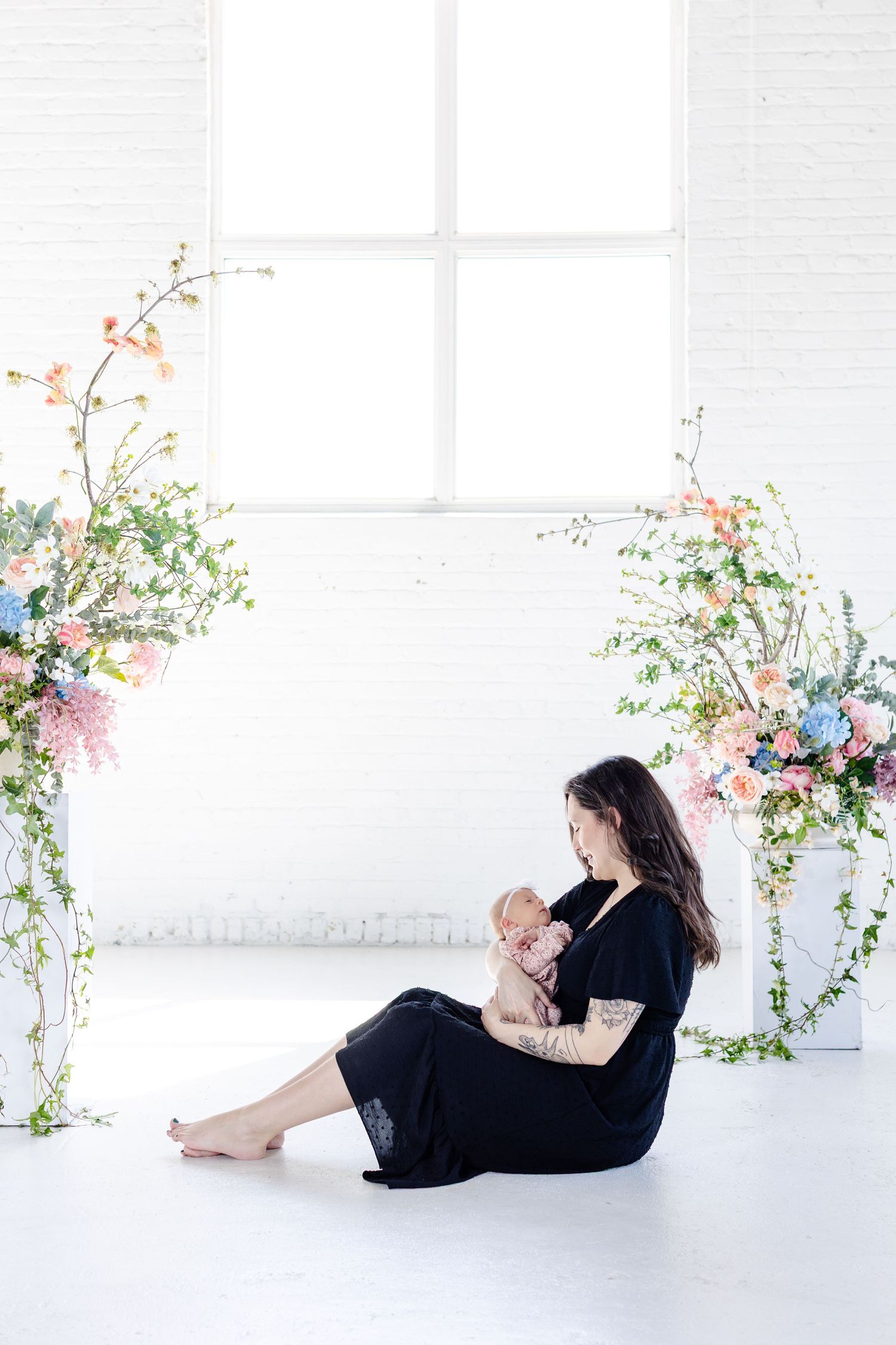 Mother wearing black dress with ling dark brown hair holding baby in pink clothes, in professional photo studio in Winnipeg for mothers  day