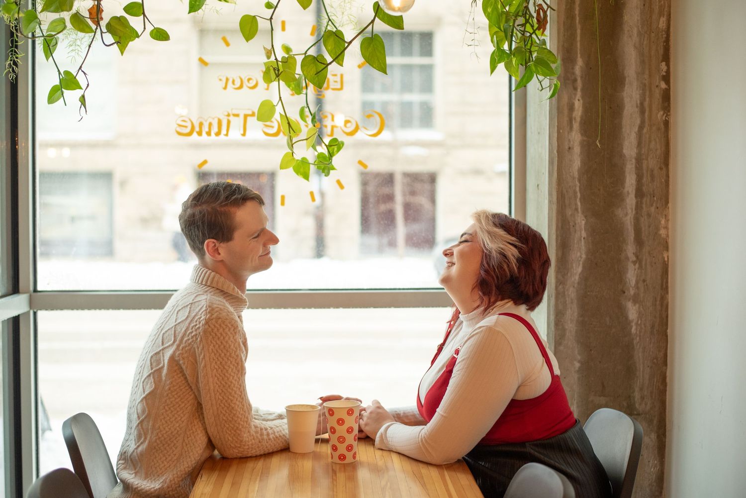 Couple smiles over coffee at winnipeg coffee shop during photoshoot