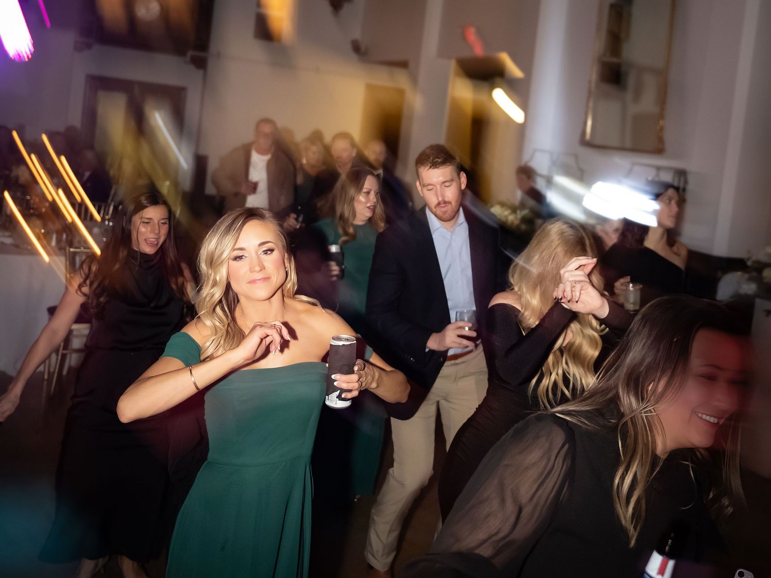 Wedding guests dancing and celebrating on a dimly lit dance floor at a reception.