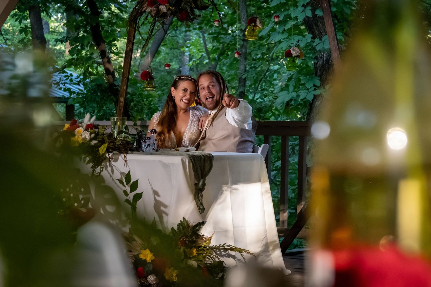 Wedding couple shares a joyful moment under a wooden arch decorated with vibrant flowers and greenery.