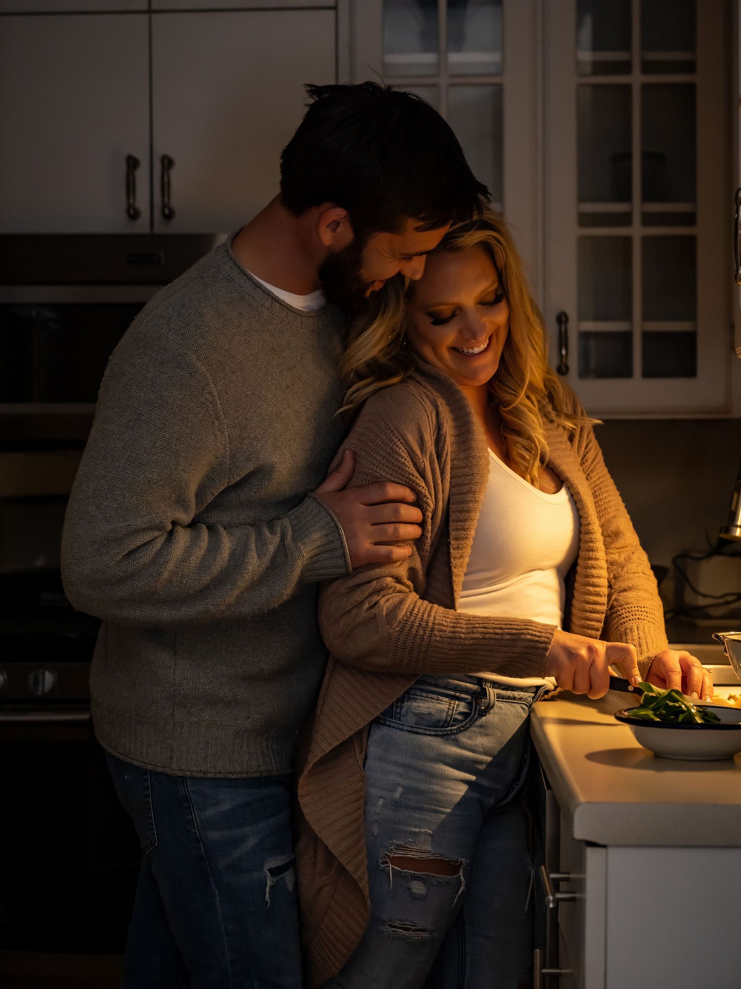 Romantic couple embracing while preparing food in cozy kitchen lighting.
