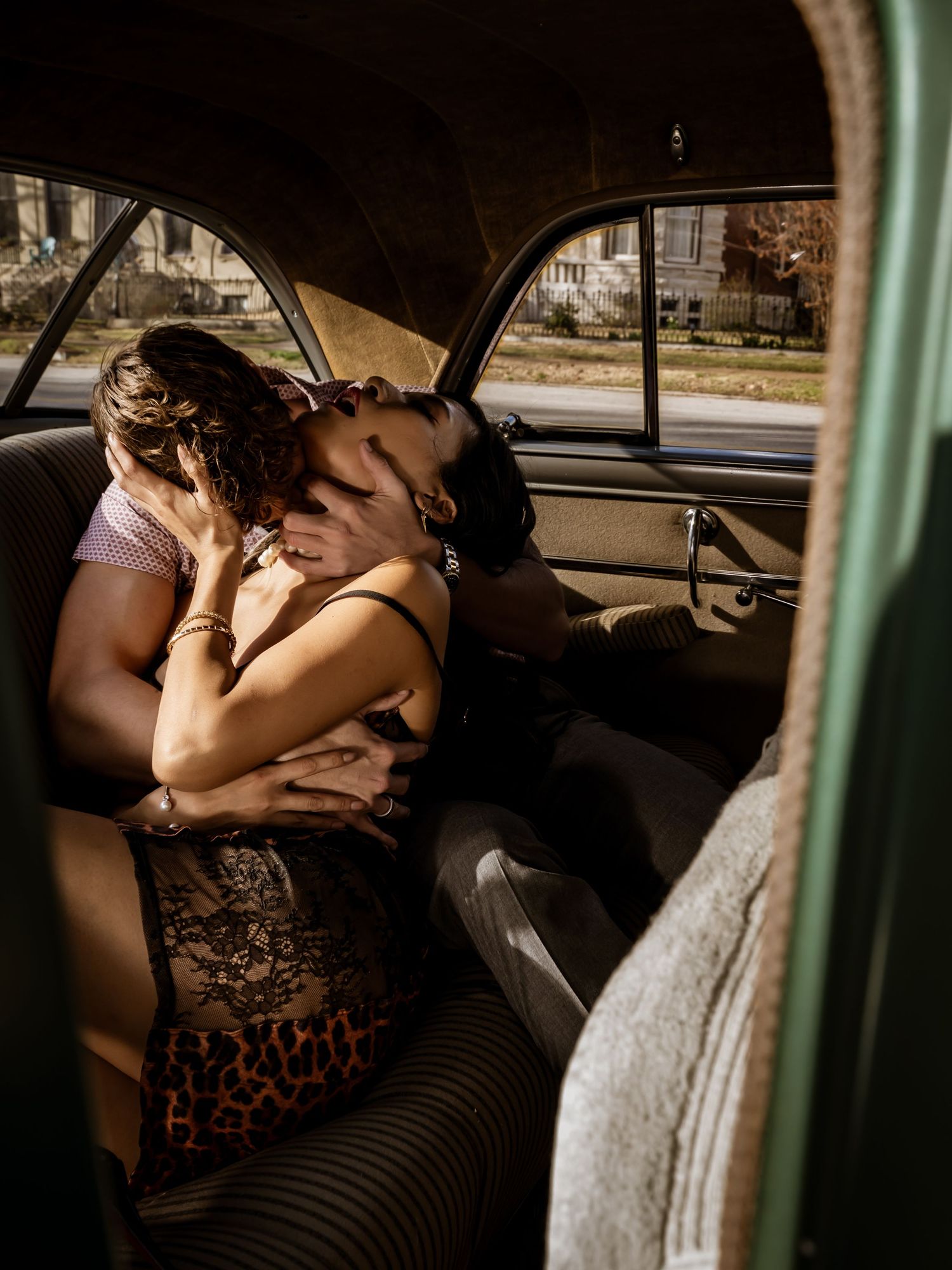 Couple sharing a passionate kiss in the backseat of a vintage classic car on a sunny day.
