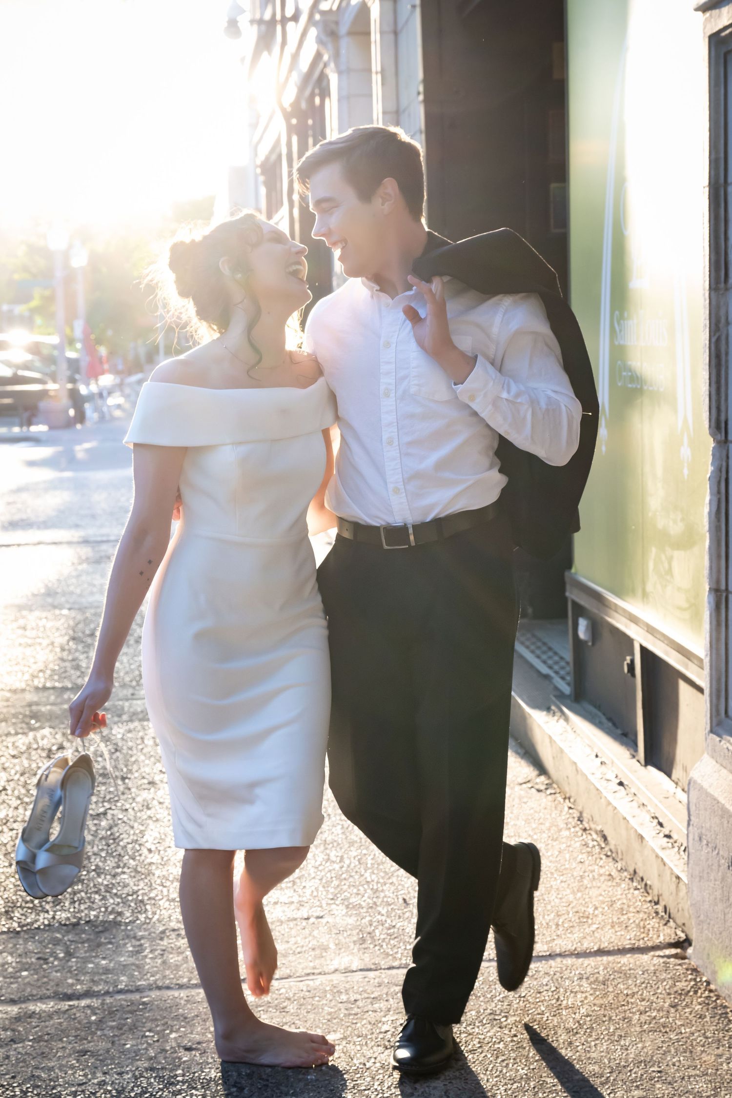 A couple in formal attire poses outdoors in dramatic sunlit lighting.