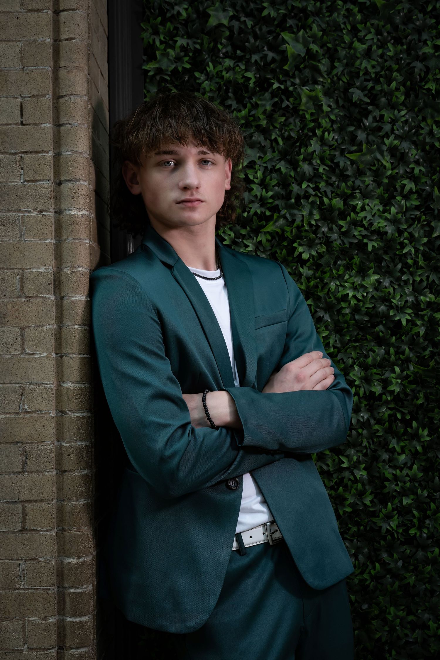 Portrait of person in green suit jacket against ivy-covered wall.