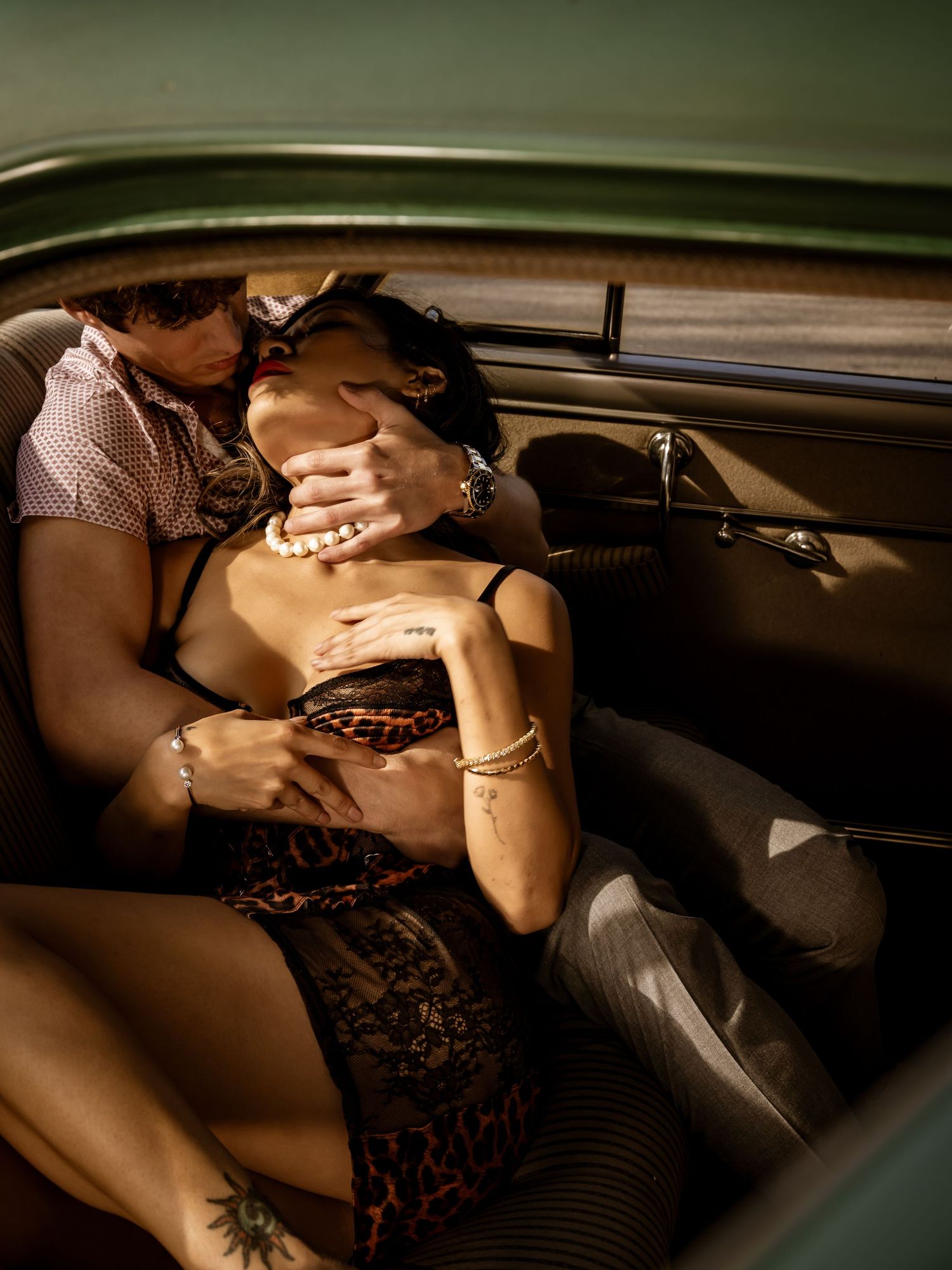 Two people sharing an intimate moment in the back seat of a vintage classic car interior.