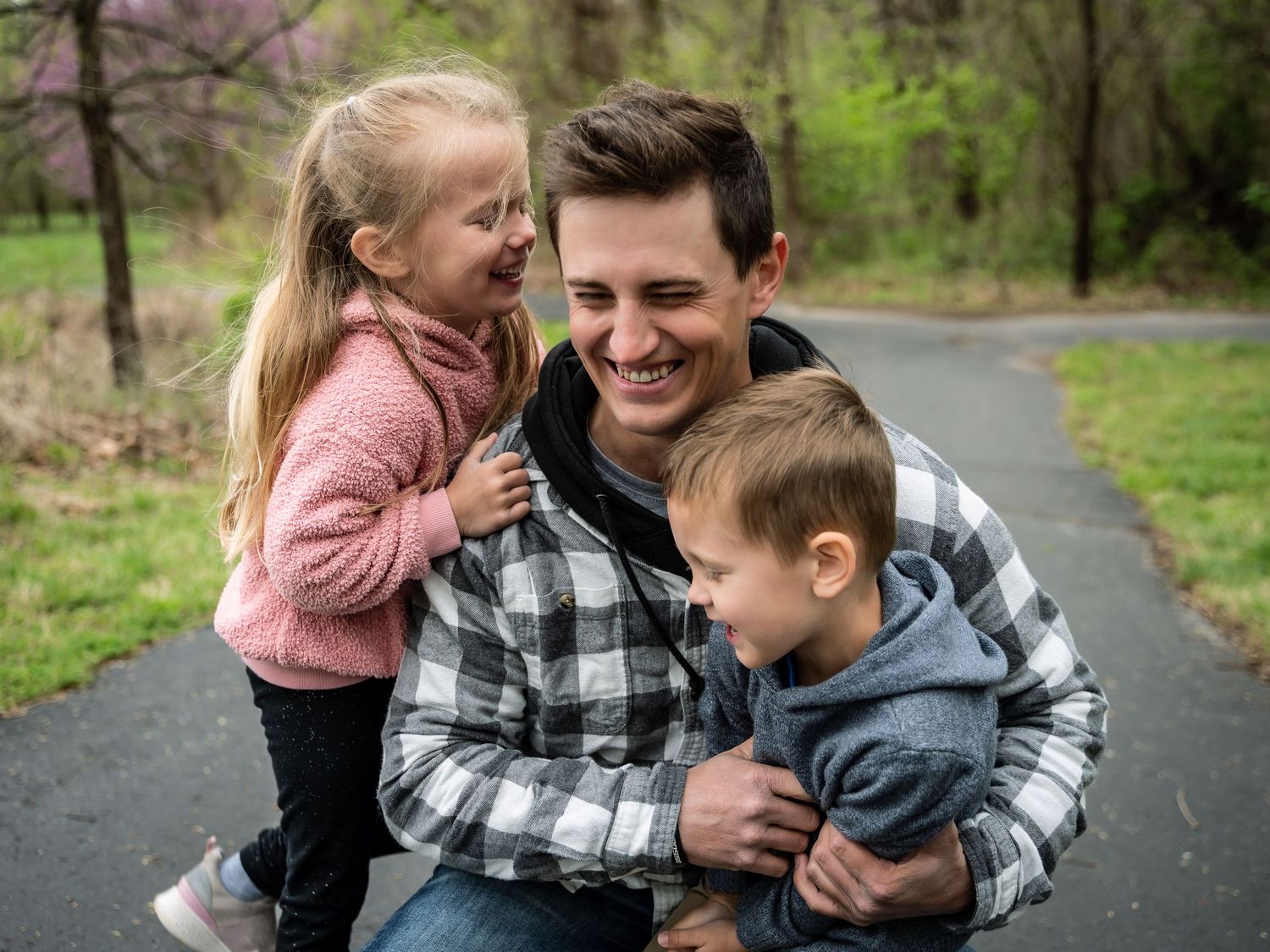 A family shares joyful moments together while sitting on a path surrounded by greenery in a park setting.