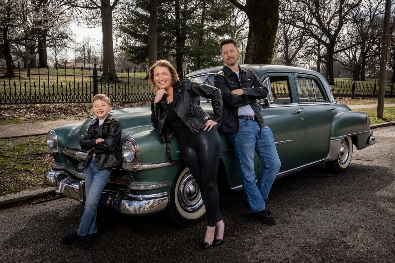 Retro themed family portrait with vintage car in park setting.