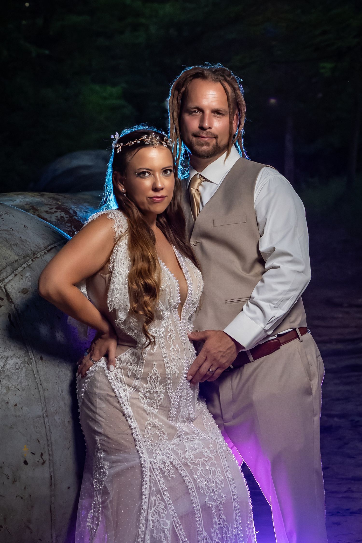 Evening wedding portraits with dramatic purple lighting against a stone backdrop.
