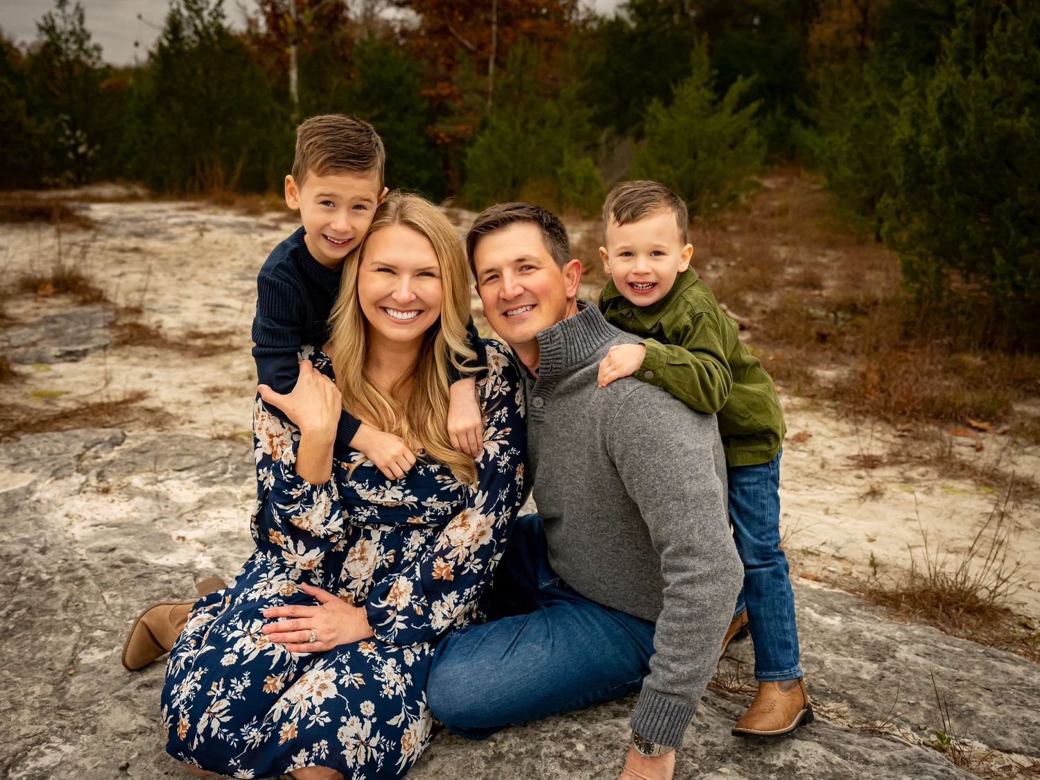 A couple in casual attire poses together outdoors during a maternity photo session in a natural setting.