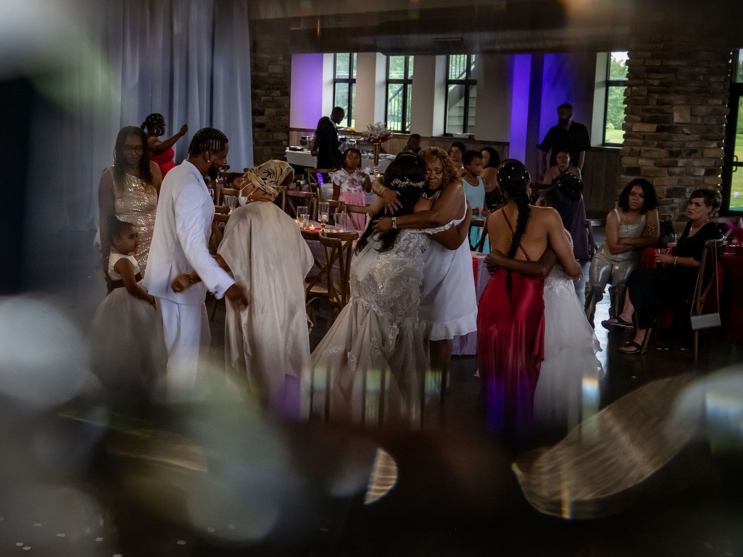 Wedding guests dancing and celebrating on a dance floor with purple lighting and white decor.