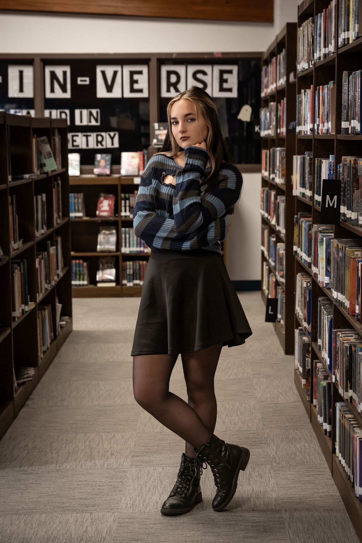 Stylish figure poses between library shelves with 'IN-VERSE' sign visible.