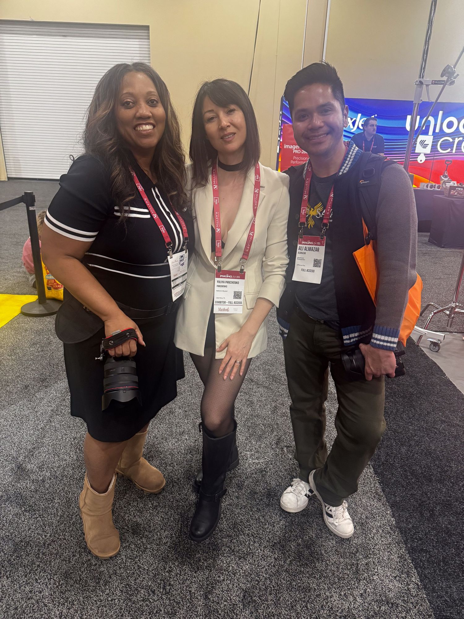 Three attendees at a conference or event posing together on a carpeted floor with a neon sign visible in the background.