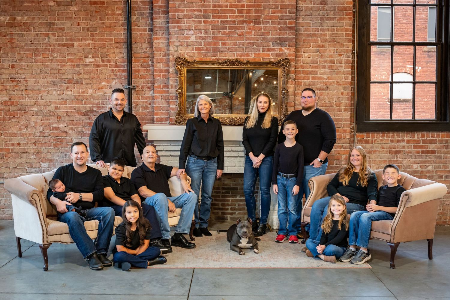 A group sits casually on a bench against a rustic brick wall in a studio-style setting.