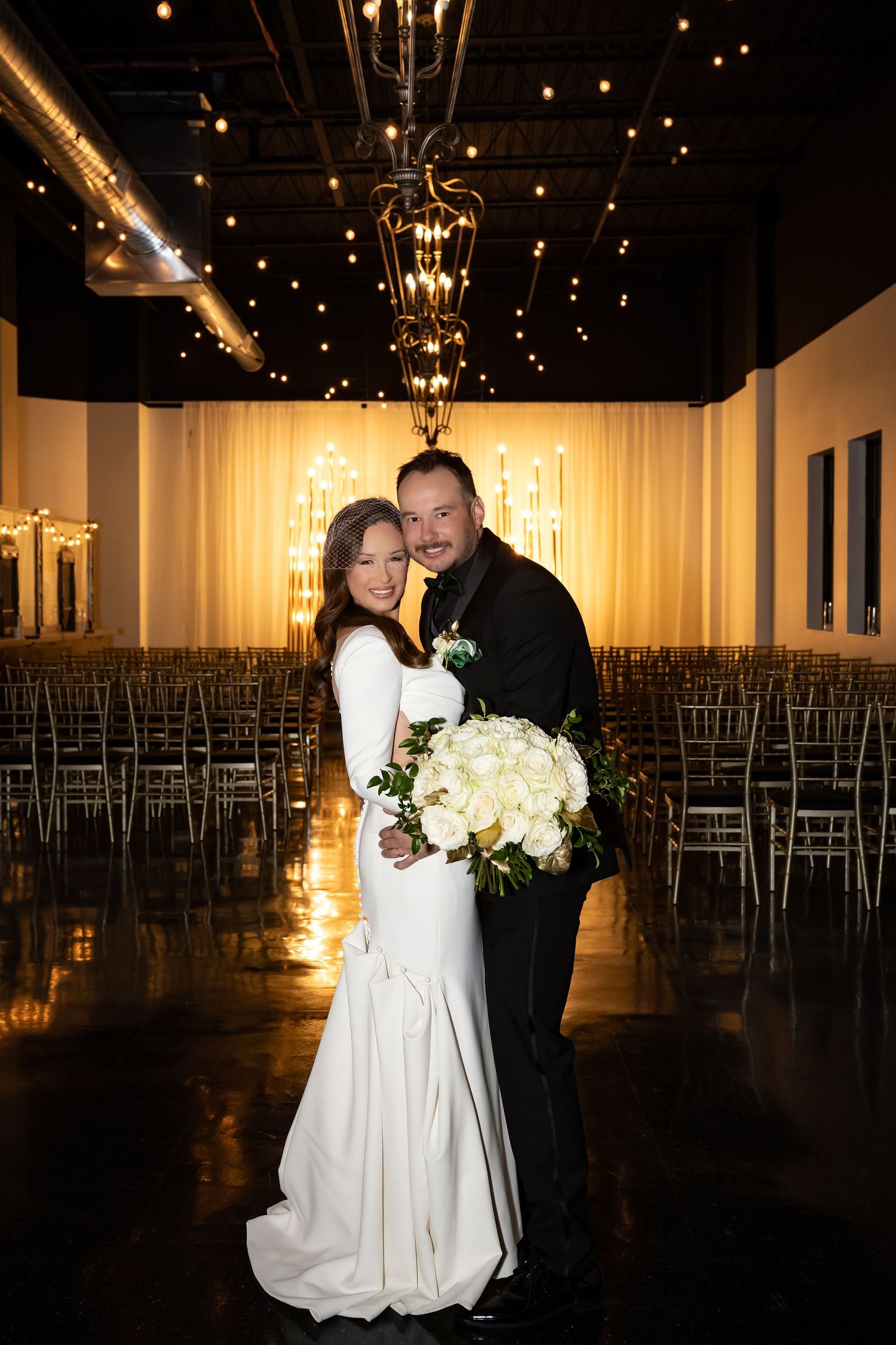 Modern wedding venue with rows of silver chairs and dramatic string light backdrop.