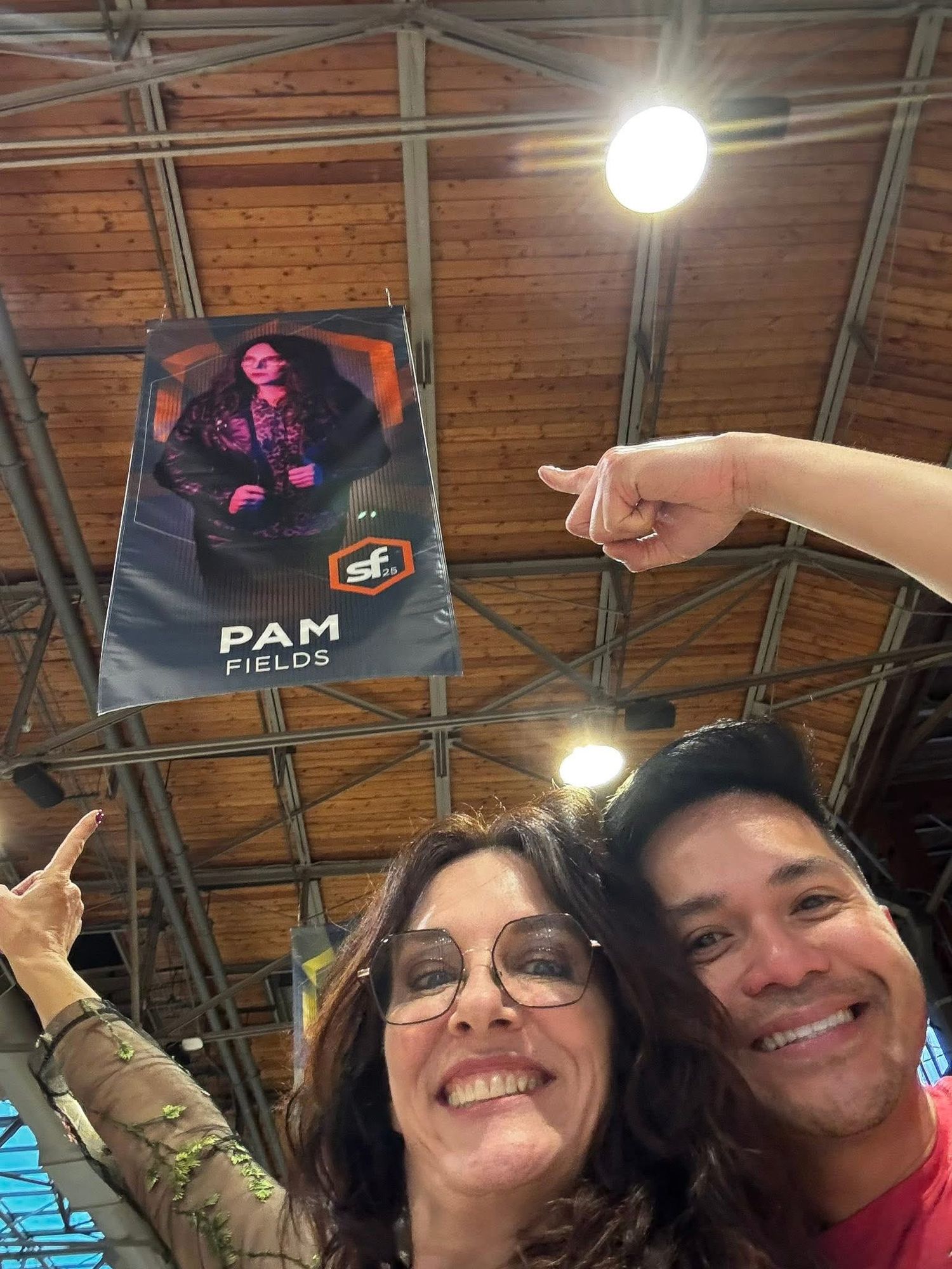 People taking selfies and smiling together inside a building with wooden ceiling beams and lighting fixtures.