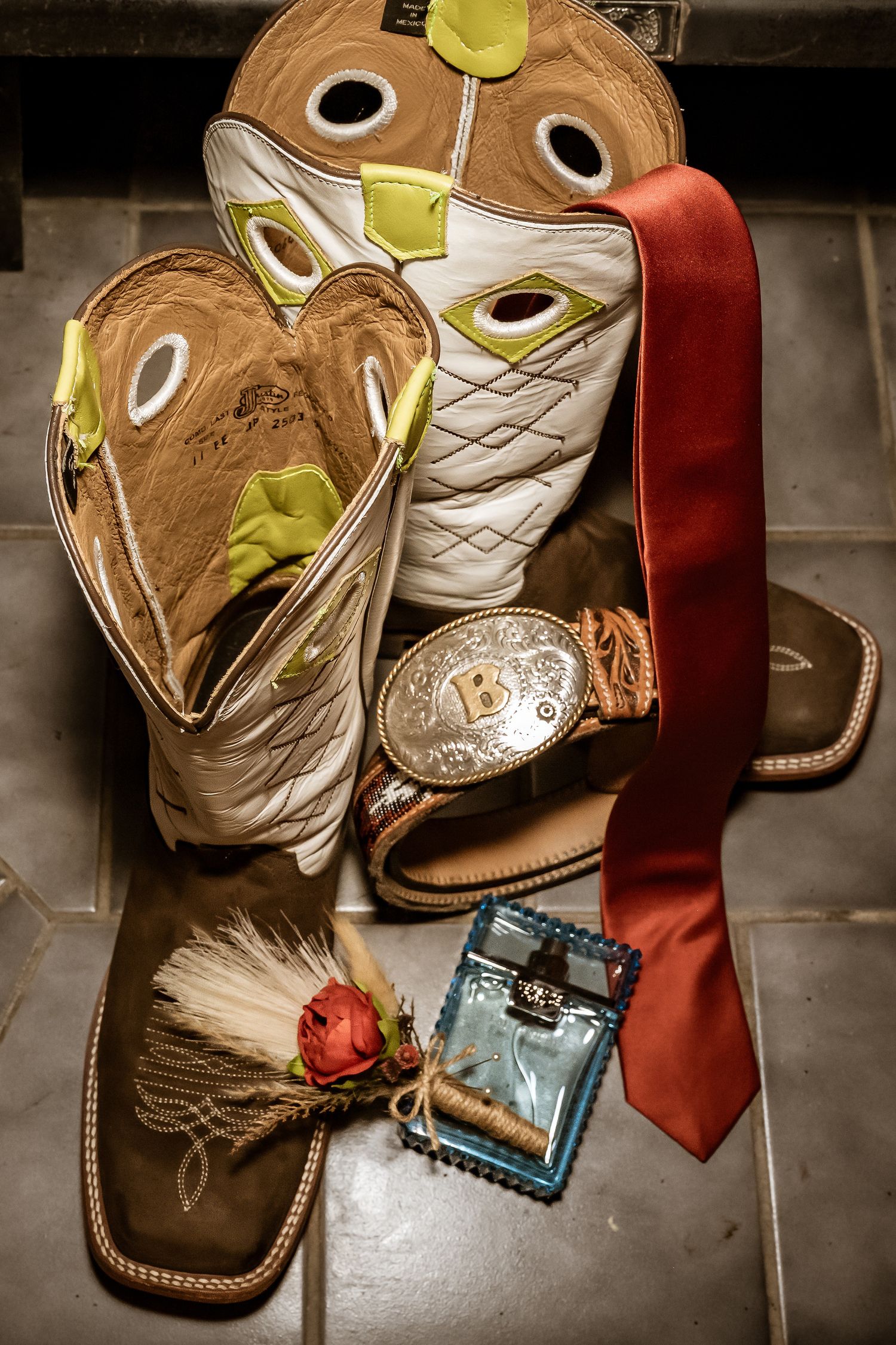 Western boots, tie, and wedding accessories arranged on a dark surface.