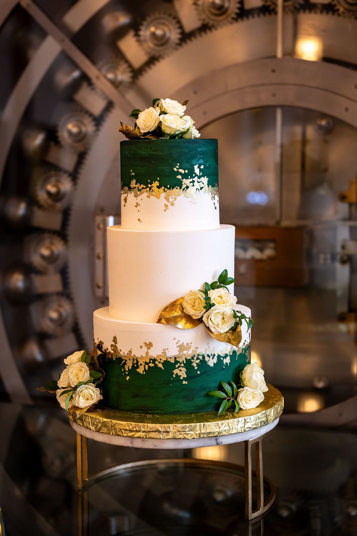 Elegant two-tier wedding cake decorated in emerald green and white with gold accents and roses.