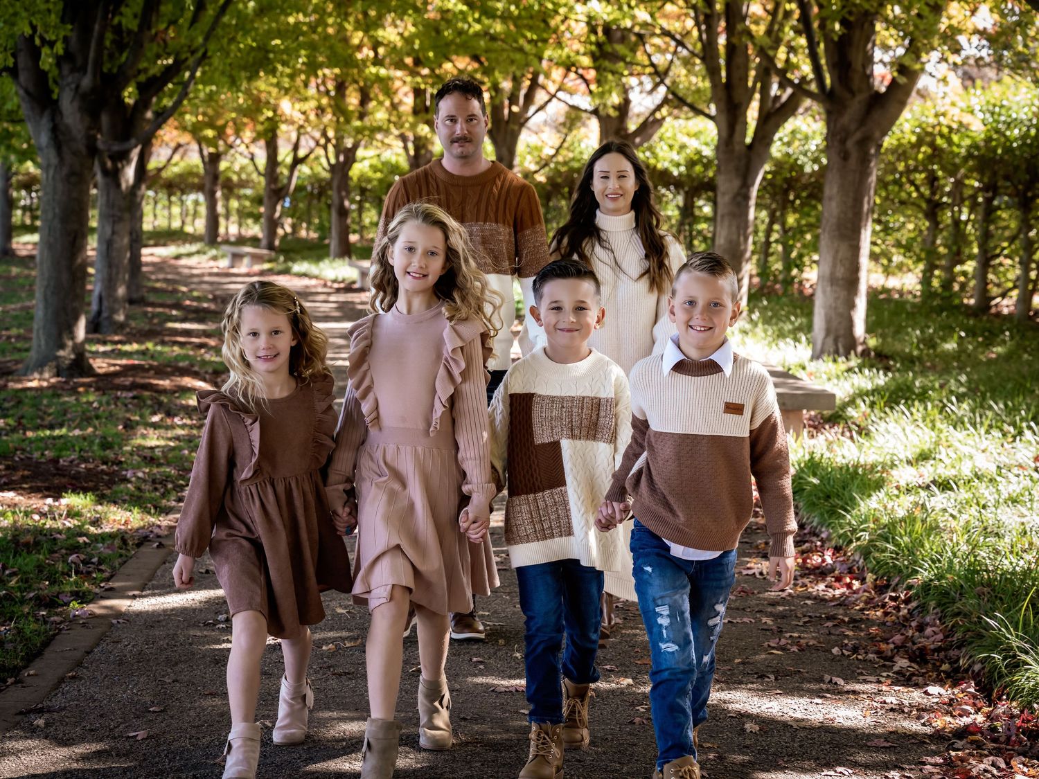 A family walking together through a sunlit wooded path during an autumn photo session.