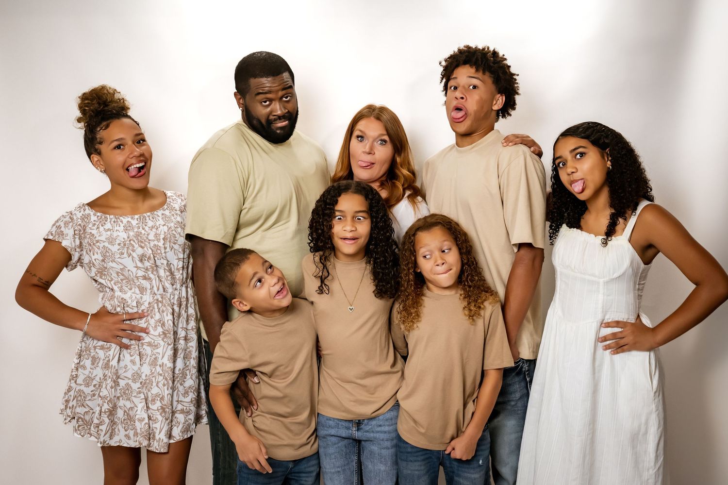 Studio portrait of diverse family group in coordinated neutral outfits against white background.