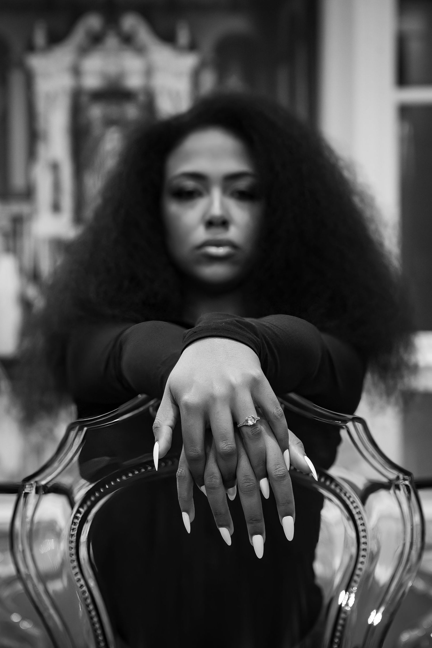 Dramatic black and white portrait with ornate chair and moody lighting.