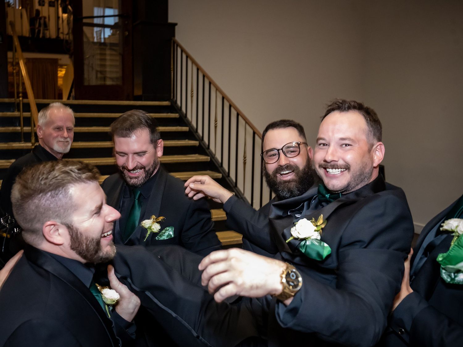 Groomsmen in black suits sharing laughs and embraces during wedding celebrations.