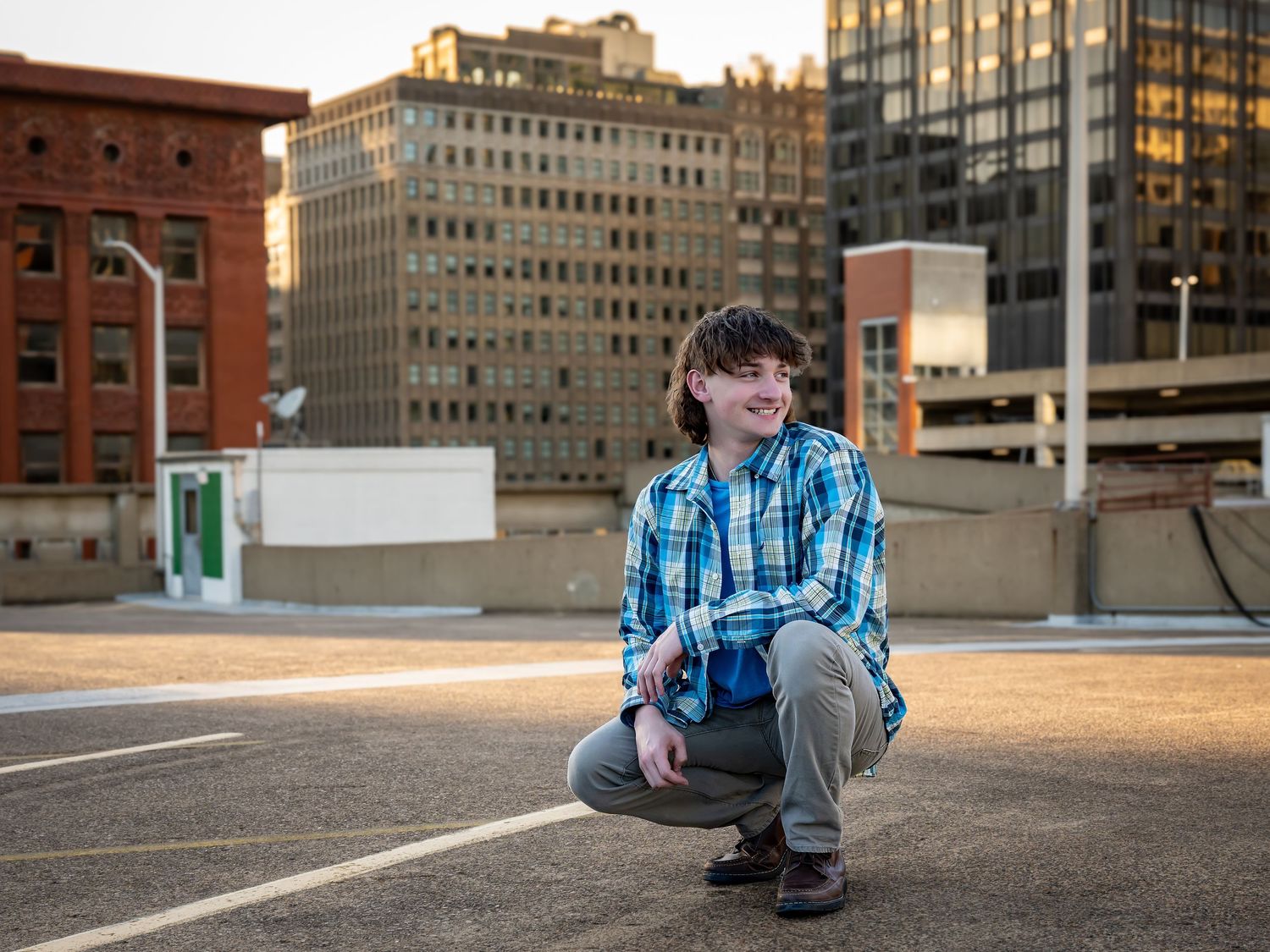 Person crouching in urban parking lot with city buildings in background at sunset.