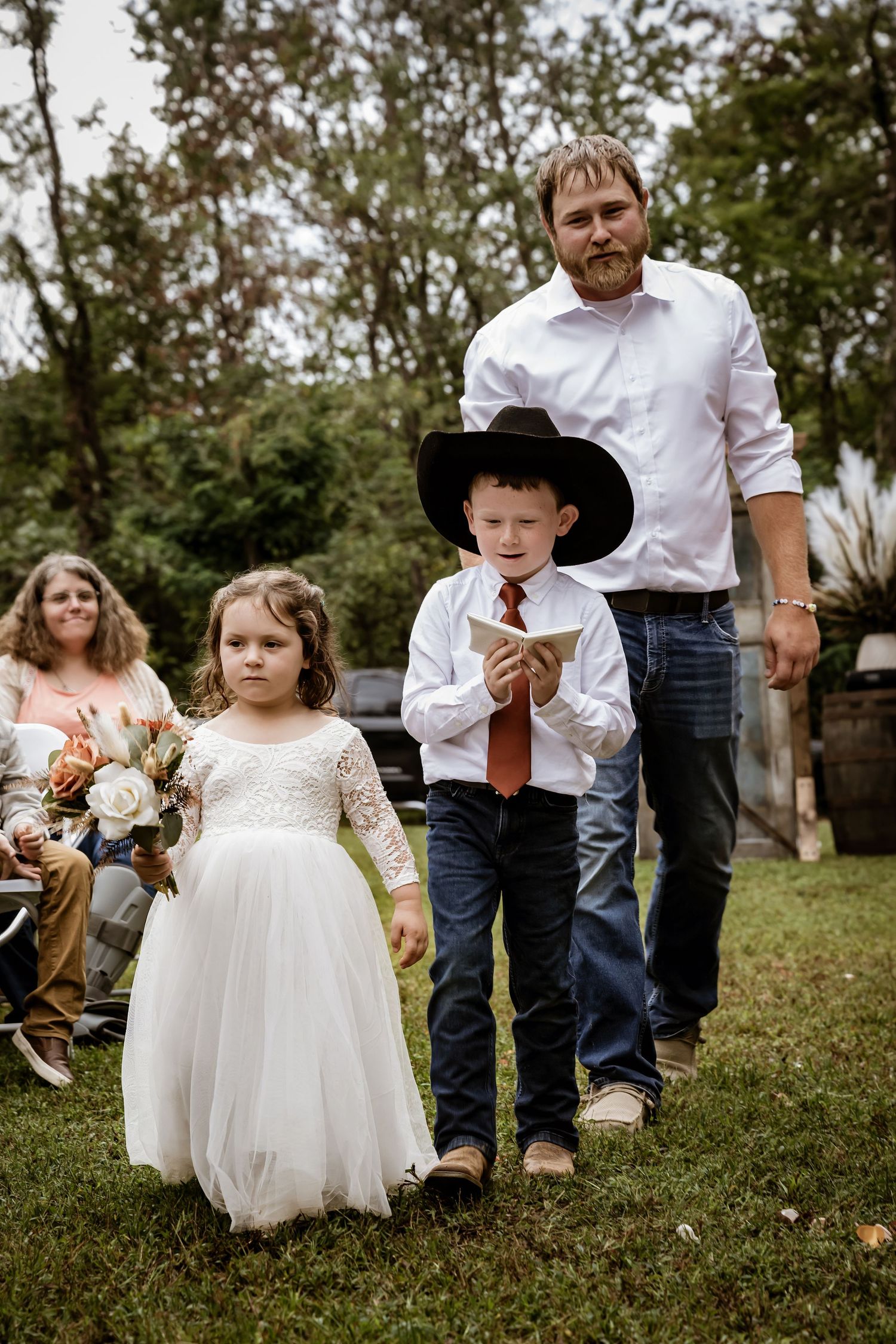 Young flower girls in white dresses play on grassy lawn during outdoor wedding.