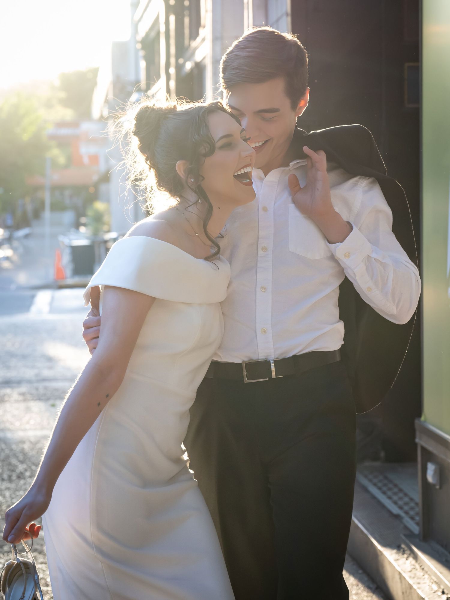 Romantic couple in formal wear sharing a playful moment in natural sunlight.