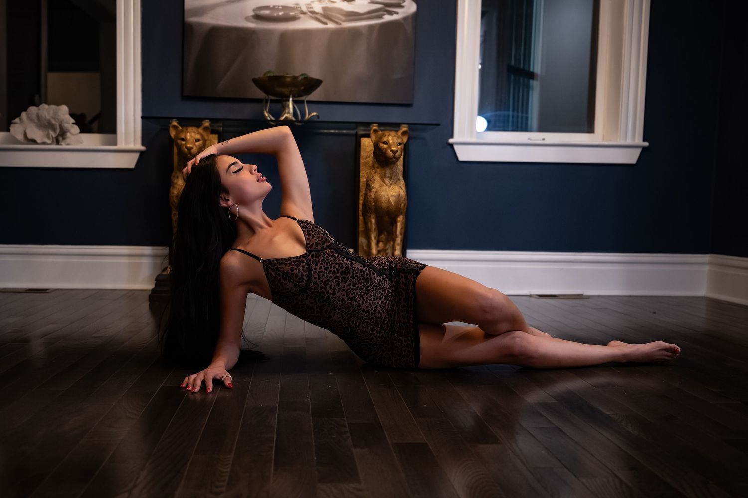 A dancer in a black outfit performs a contemporary dance pose on a dark hardwood floor.