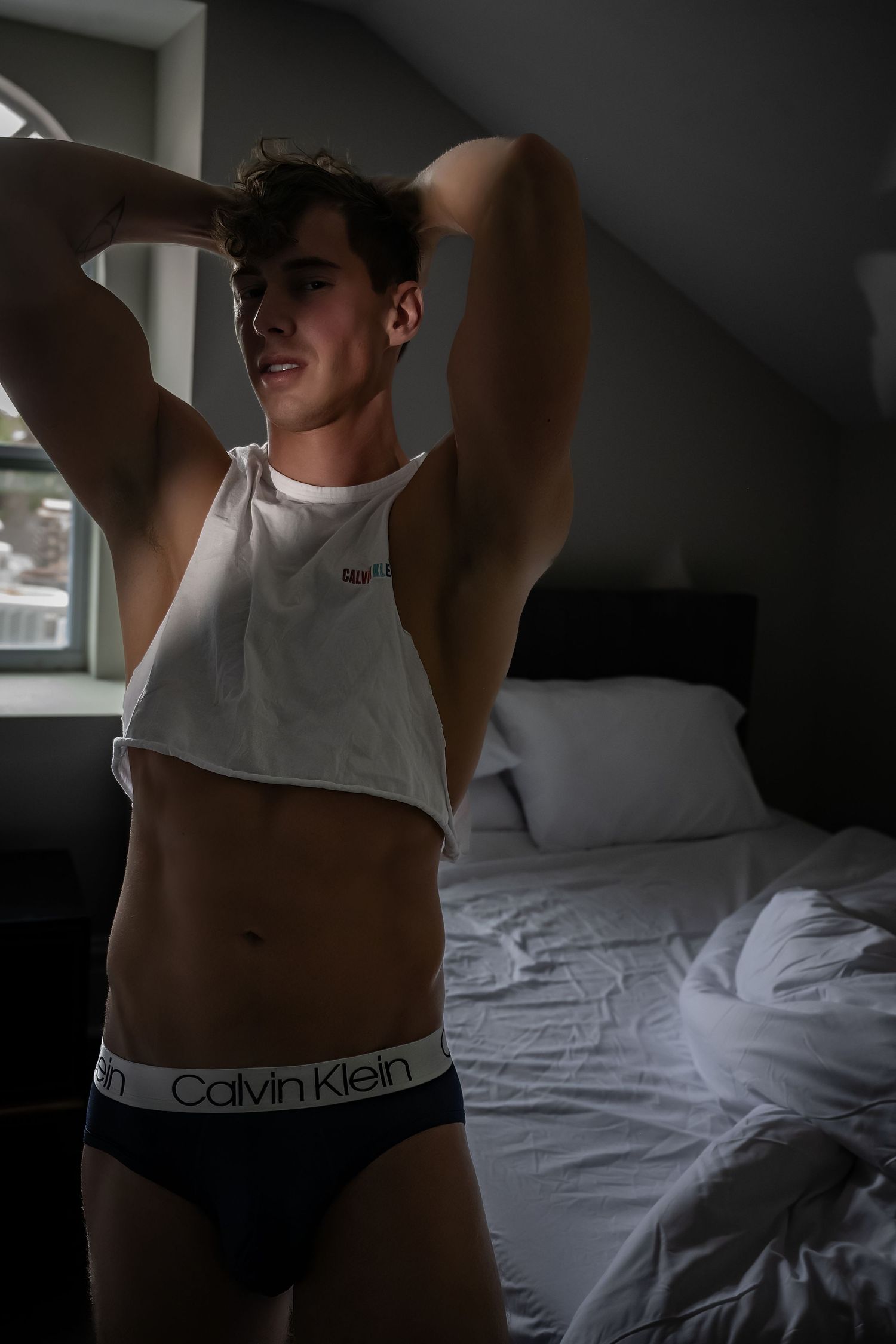 Artistic black and white photos showing a person in Calvin Klein underwear lounging on white bedding.