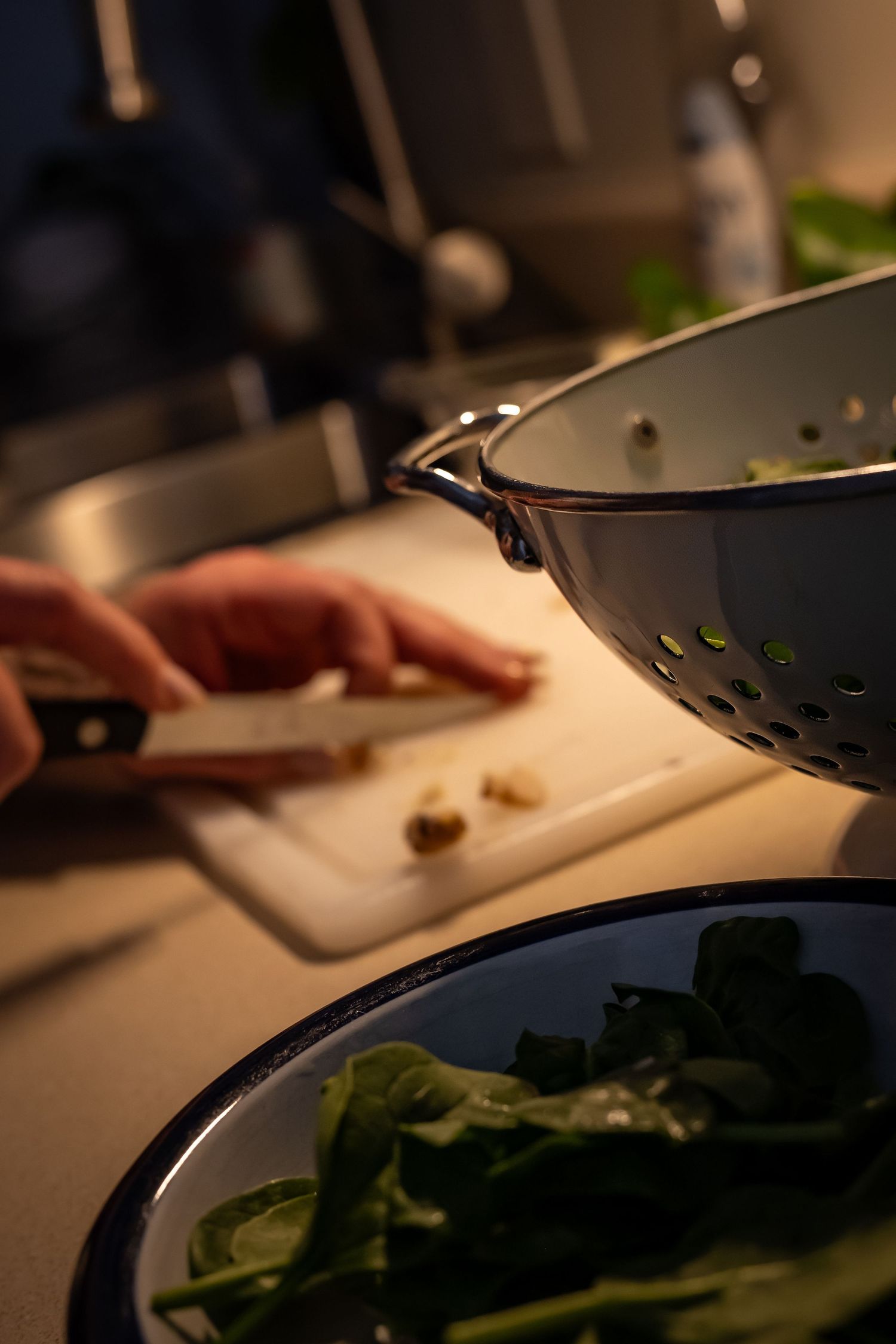 Hands chopping vegetables on a cutting board in moody kitchen lighting.