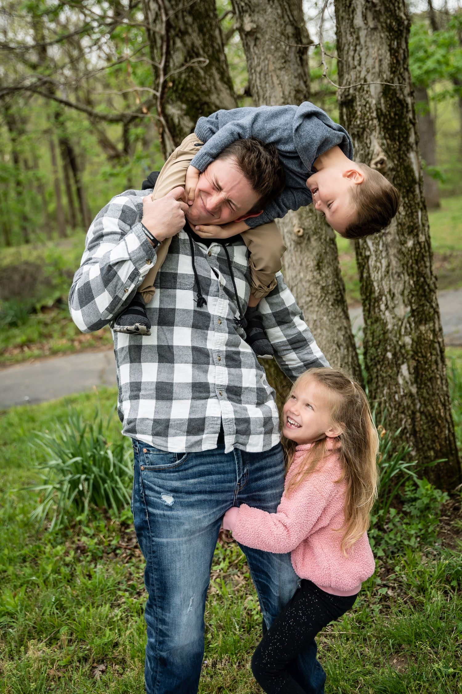 Joyful outdoor portrait showing playful interaction between parent and children by trees.