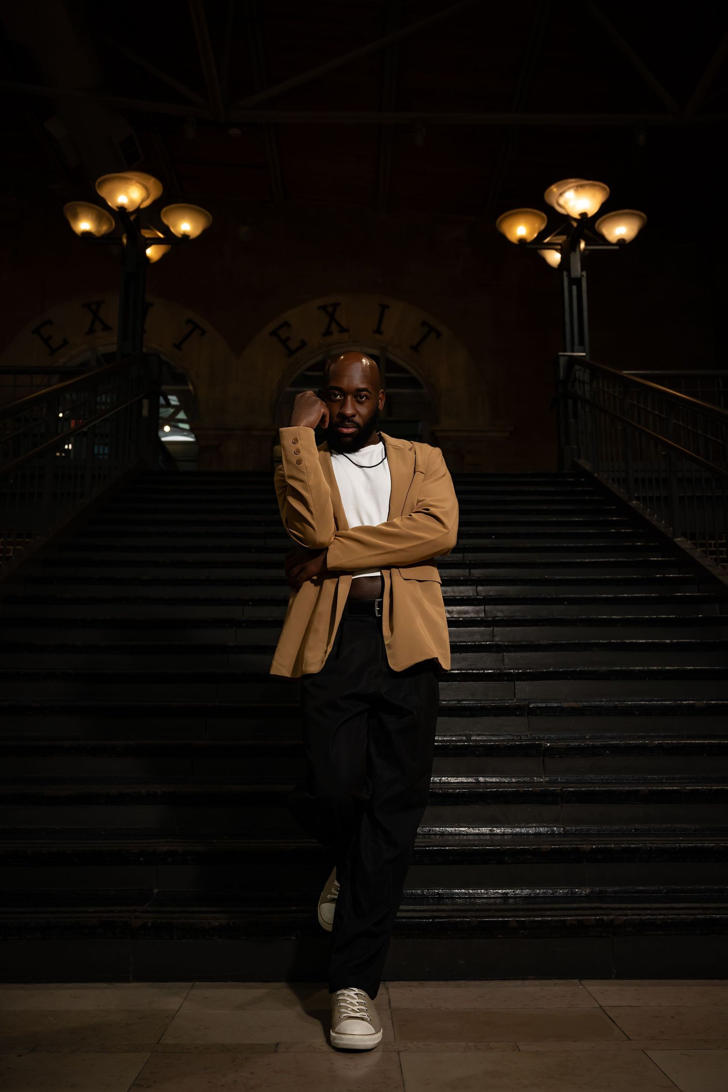 Dramatic nighttime portrait on stone steps with moody lighting and tan blazer.