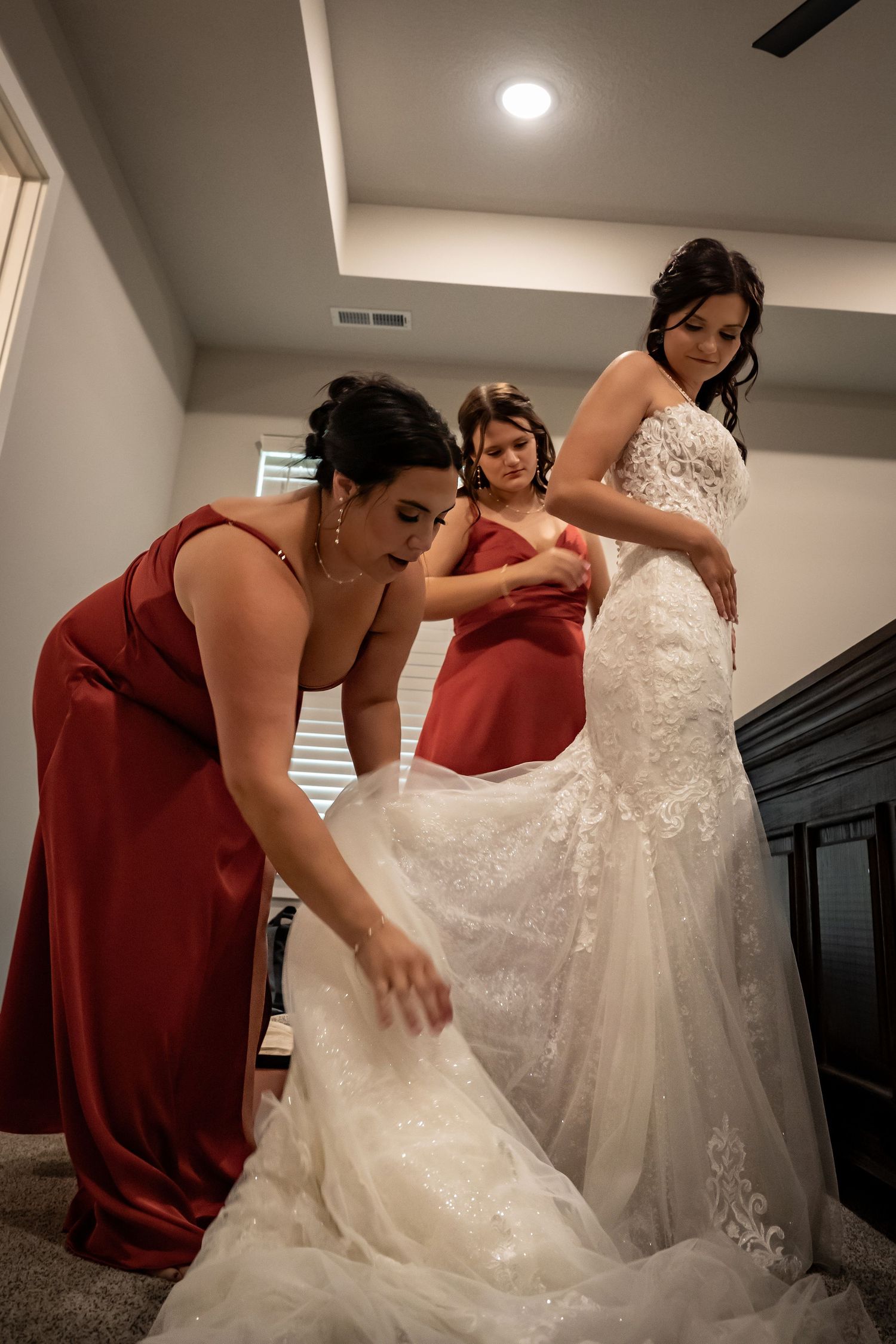 Bridesmaids in burgundy dresses help adjust wedding gown train.