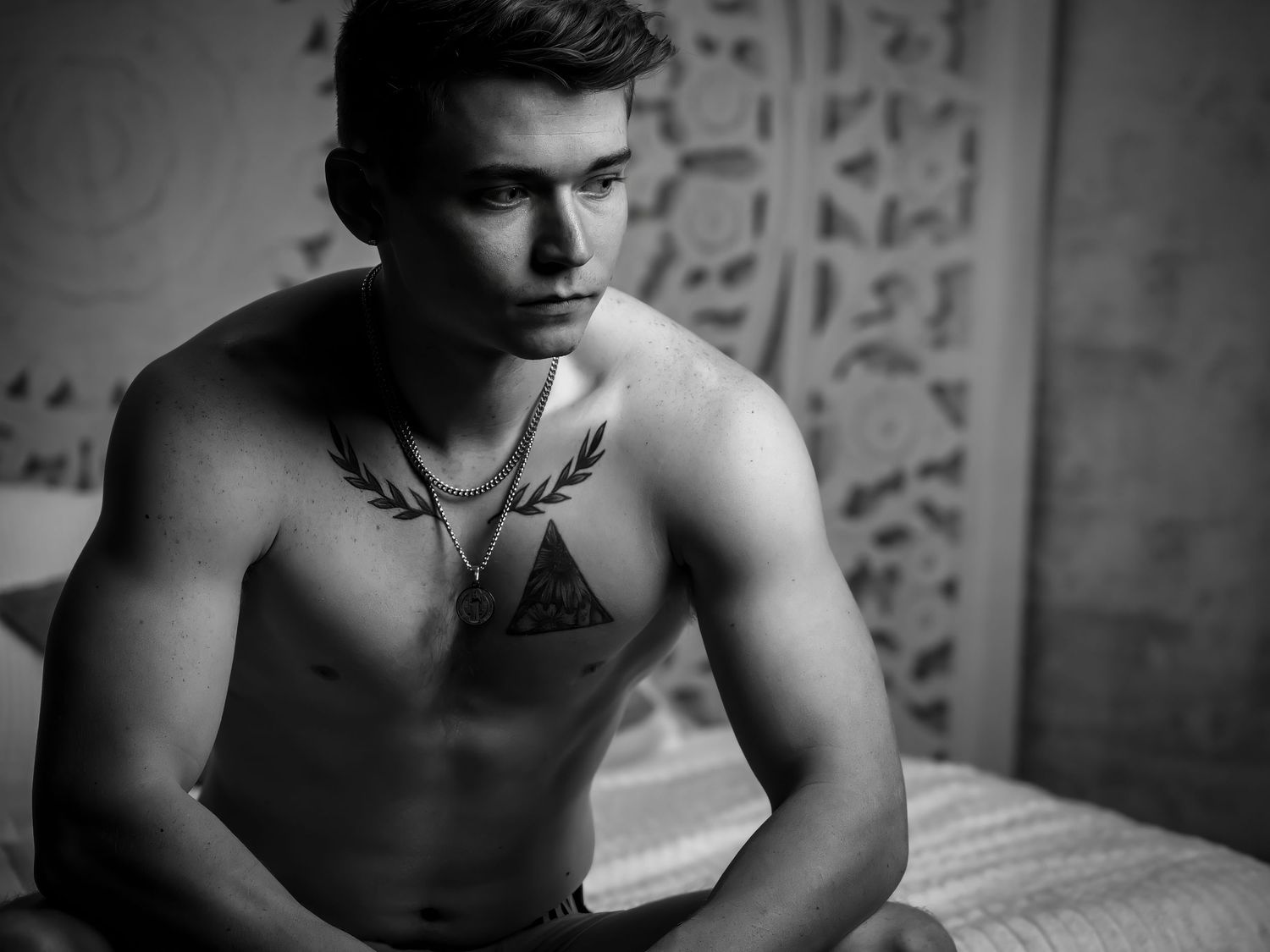 Monochrome portrait showing tattoos and muscular definition in low-key lighting.