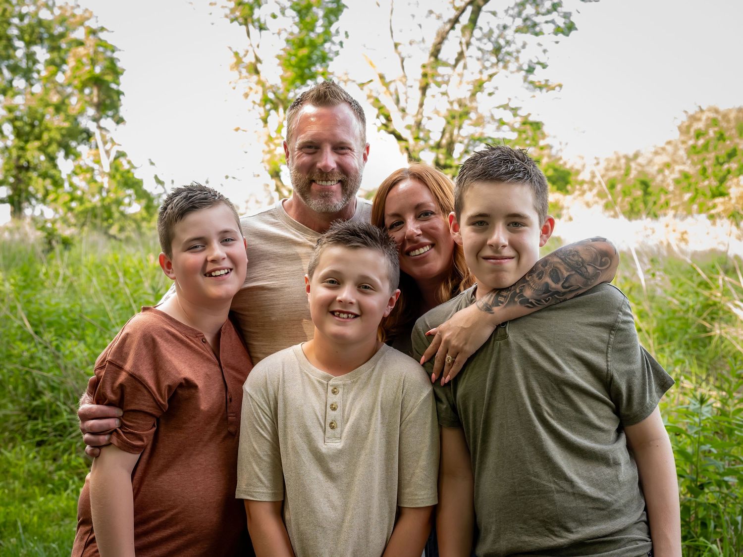 Candid family portraits captured in a natural outdoor setting with green foliage.