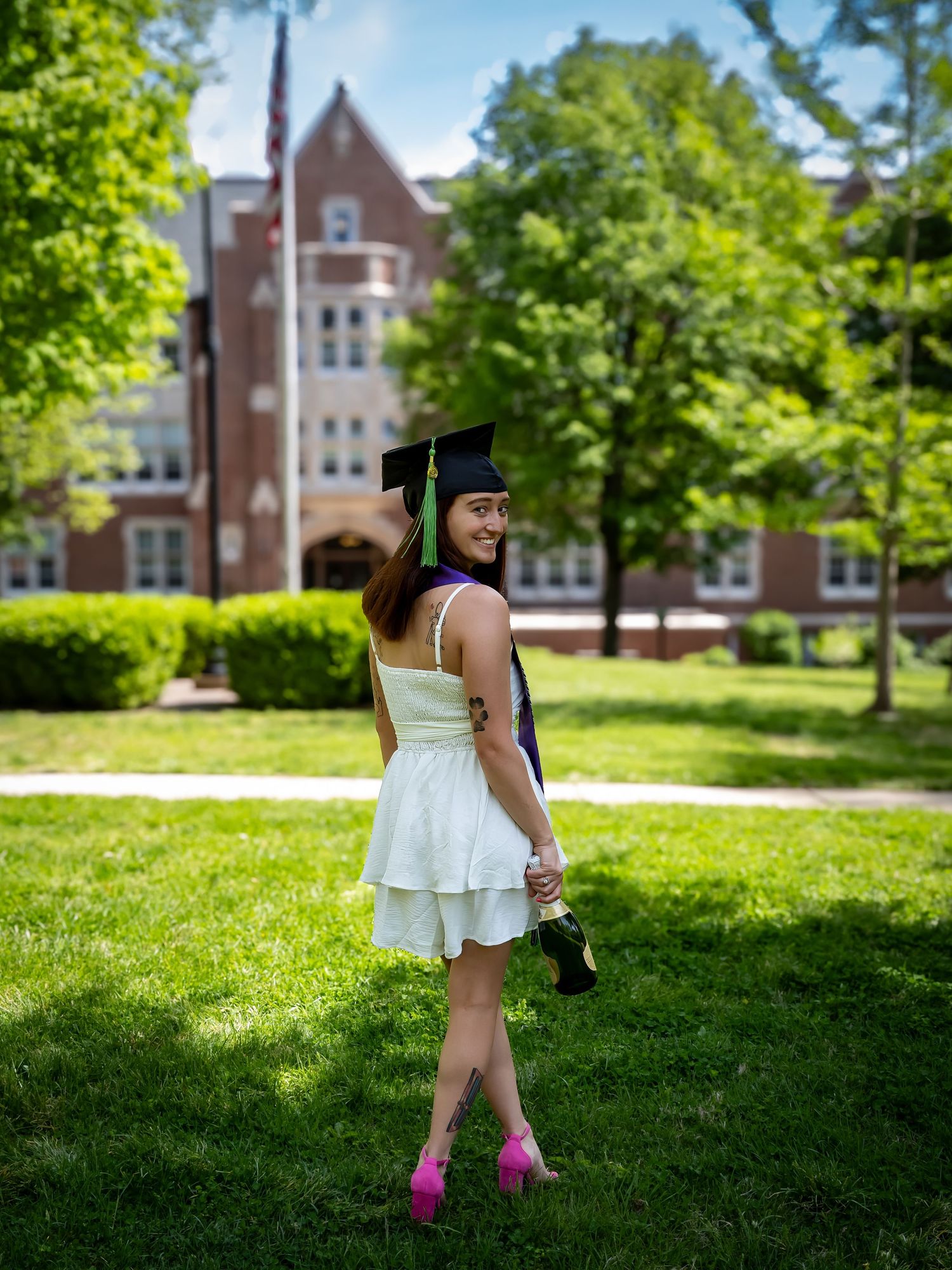 Playful graduation poses on a sunny college campus with brick buildings in background.