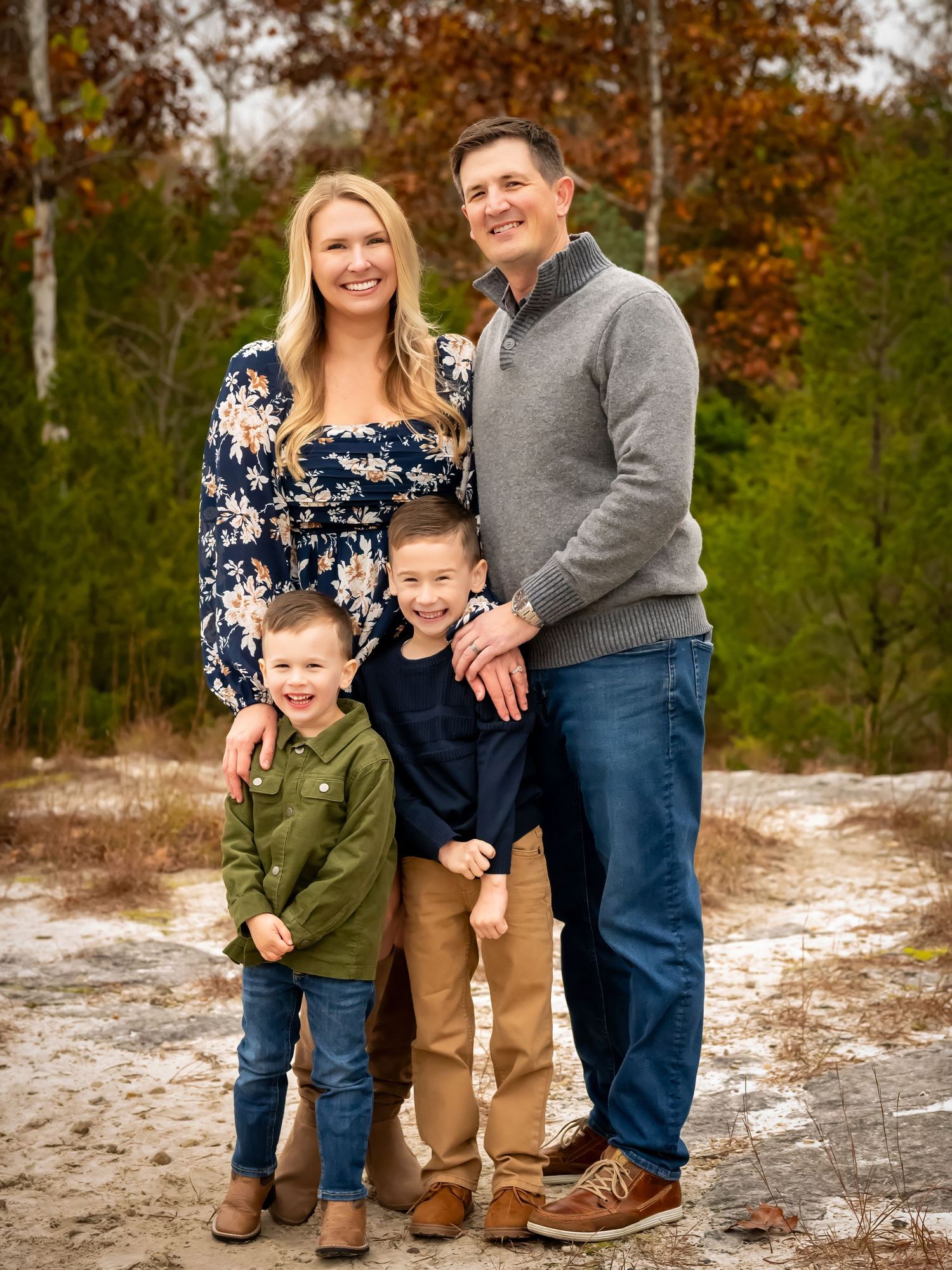 A winter family photo session with snow-covered ground and autumn trees in the background.