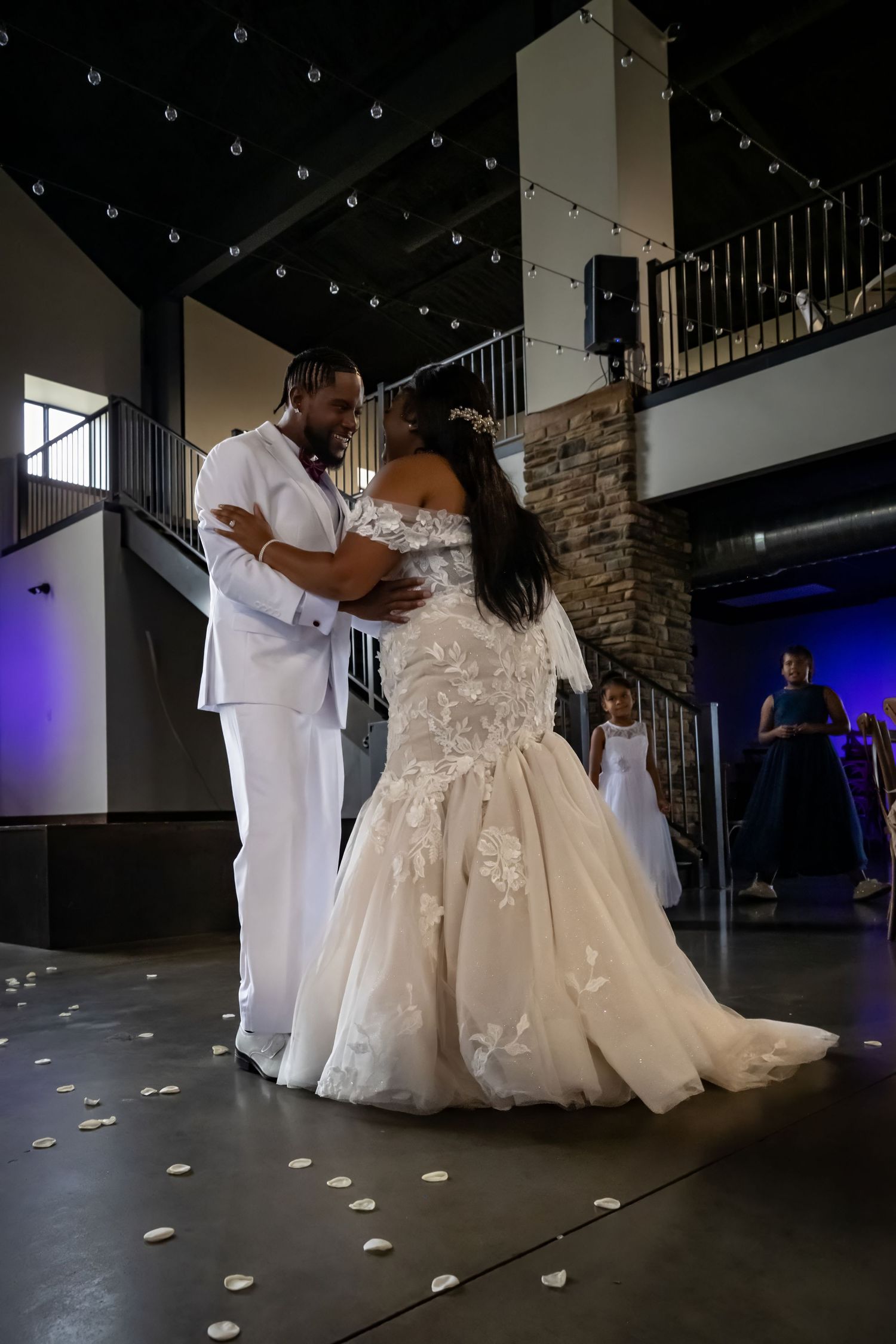 Low angle view of couple dancing on dark floor with scattered rose petals and mood lighting.