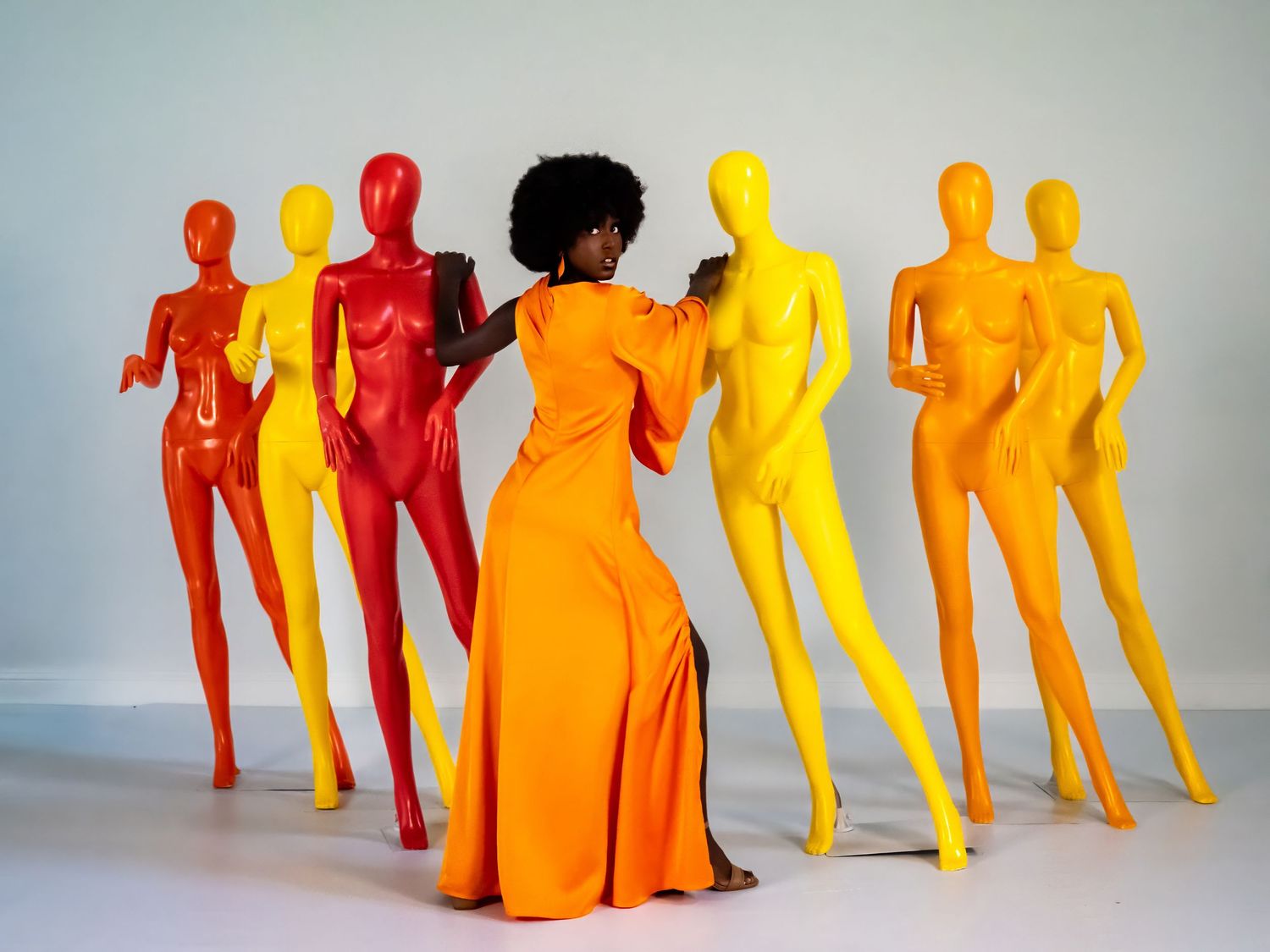 Artistic arrangement of colorful mannequins in red, yellow and orange tones against white background.