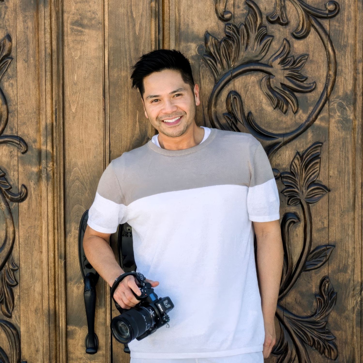 Person in white t-shirt poses against rustic wooden wall with decorative wrought iron scroll detail.