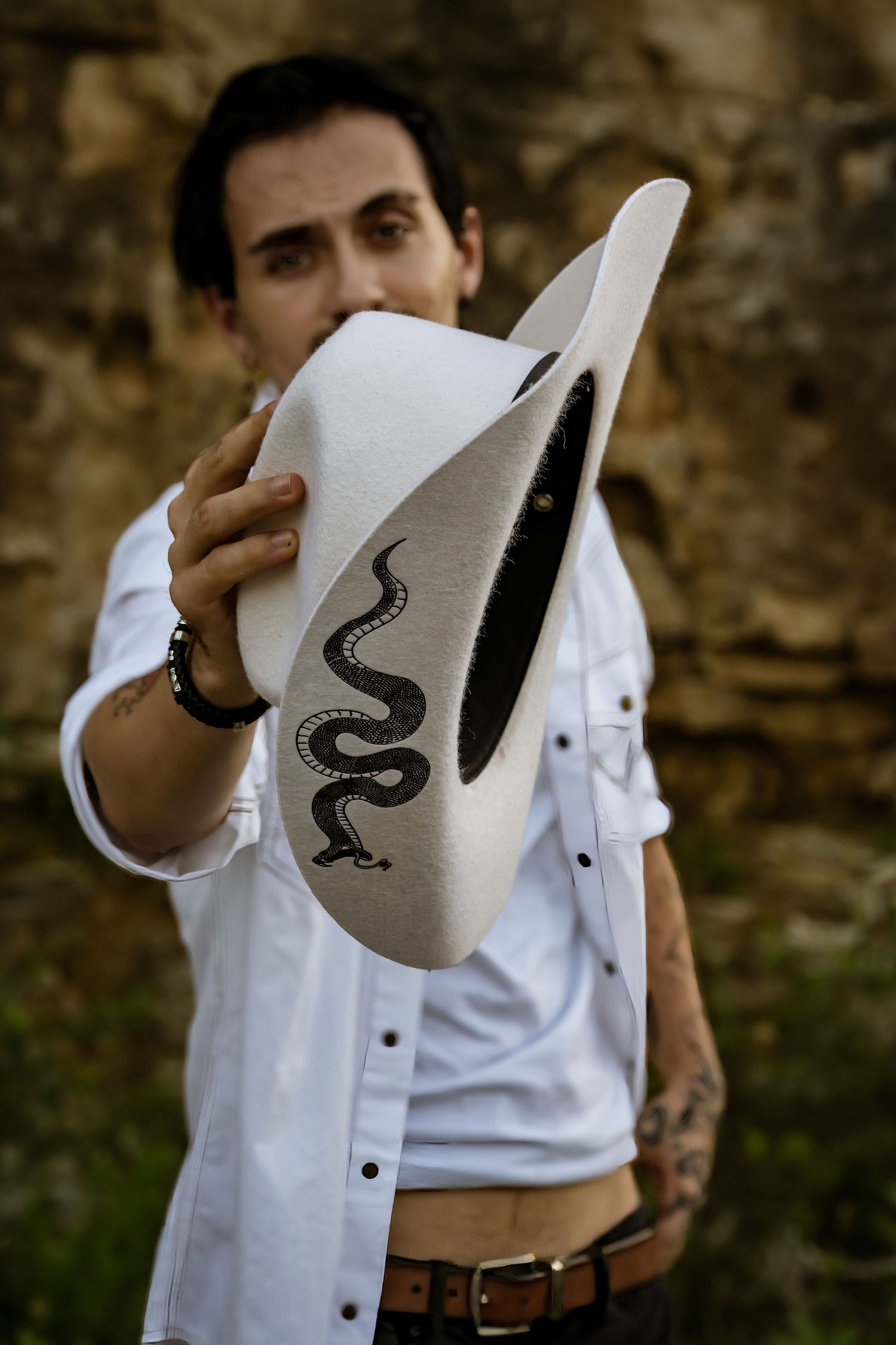 Close-up of a white cowboy hat with decorative snake design being held against rocky background.