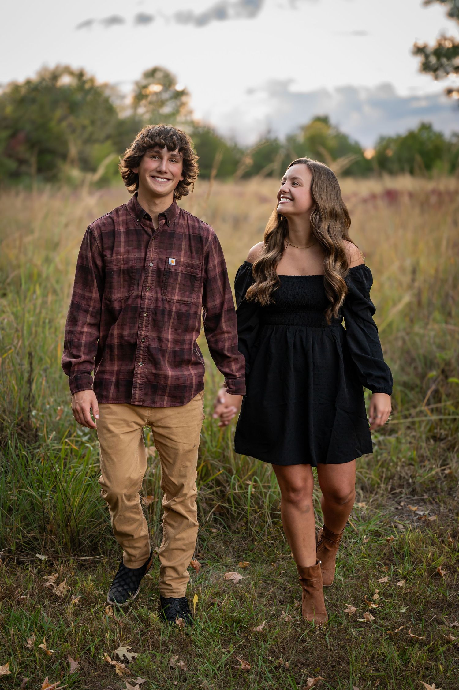 A couple walks through a grassy field on an autumn day wearing casual clothing and sharing joyful moments together.
