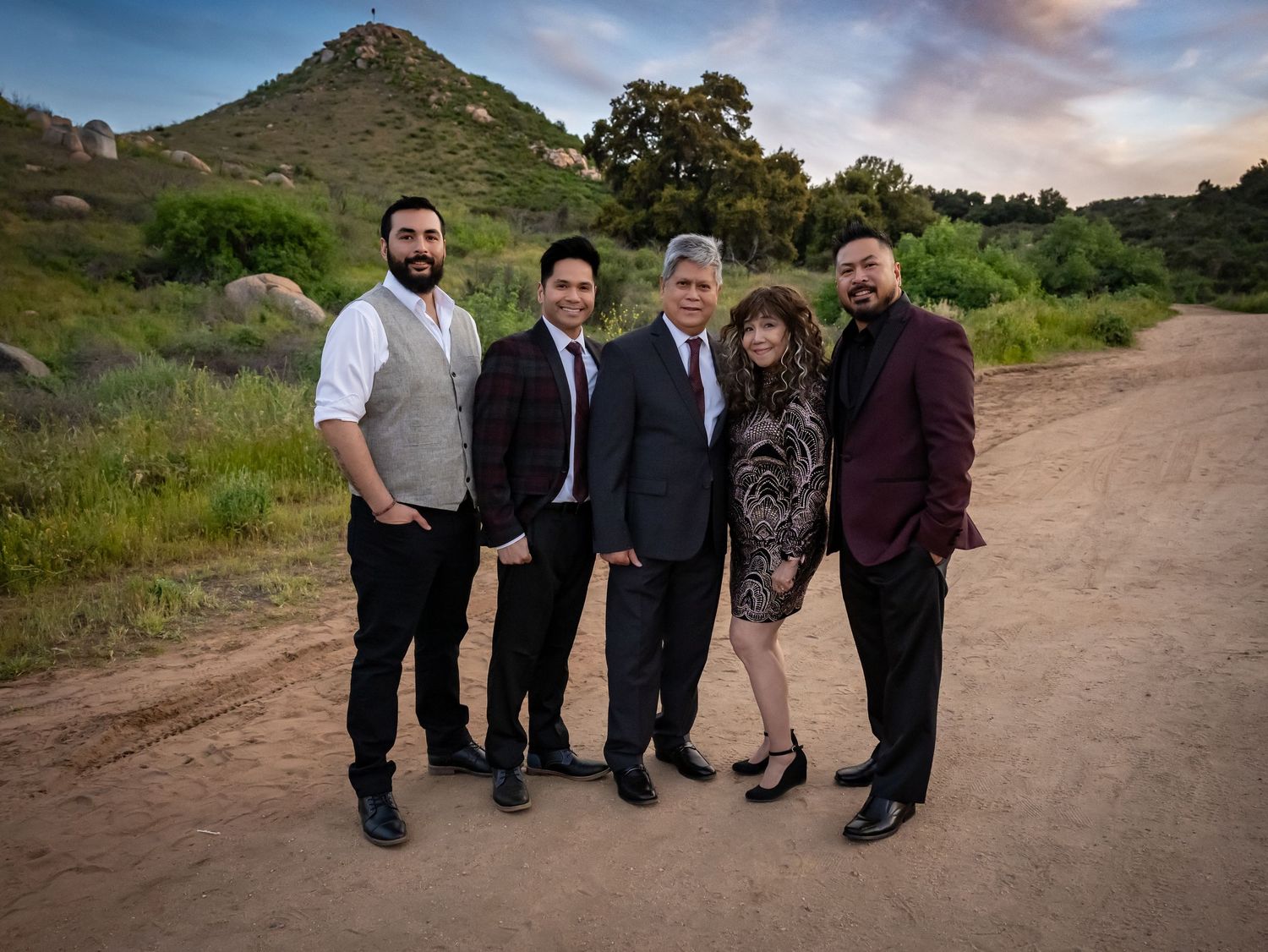 Group photo of people standing together on dirt path with mountain backdrop at sunset.