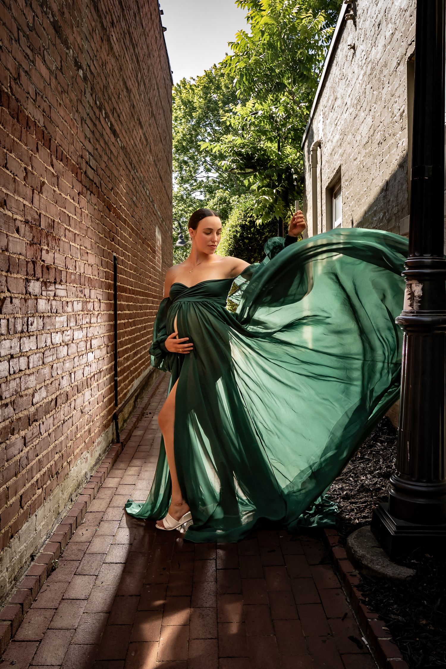 Emerald green flowing dress creates dramatic movement in narrow brick alleyway.