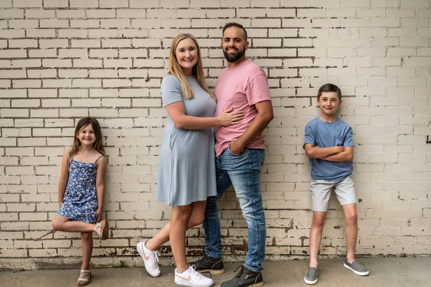 Family portrait session against a white brick wall showing casual poses and coordinated outfits.