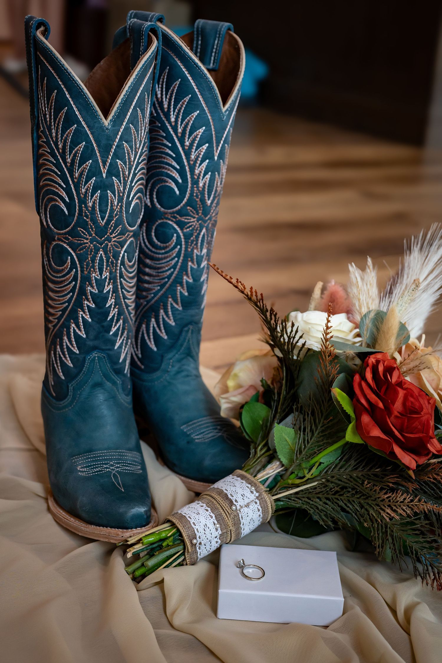 Blue cowboy boots with decorative stitching displayed next to floral arrangements and greenery.