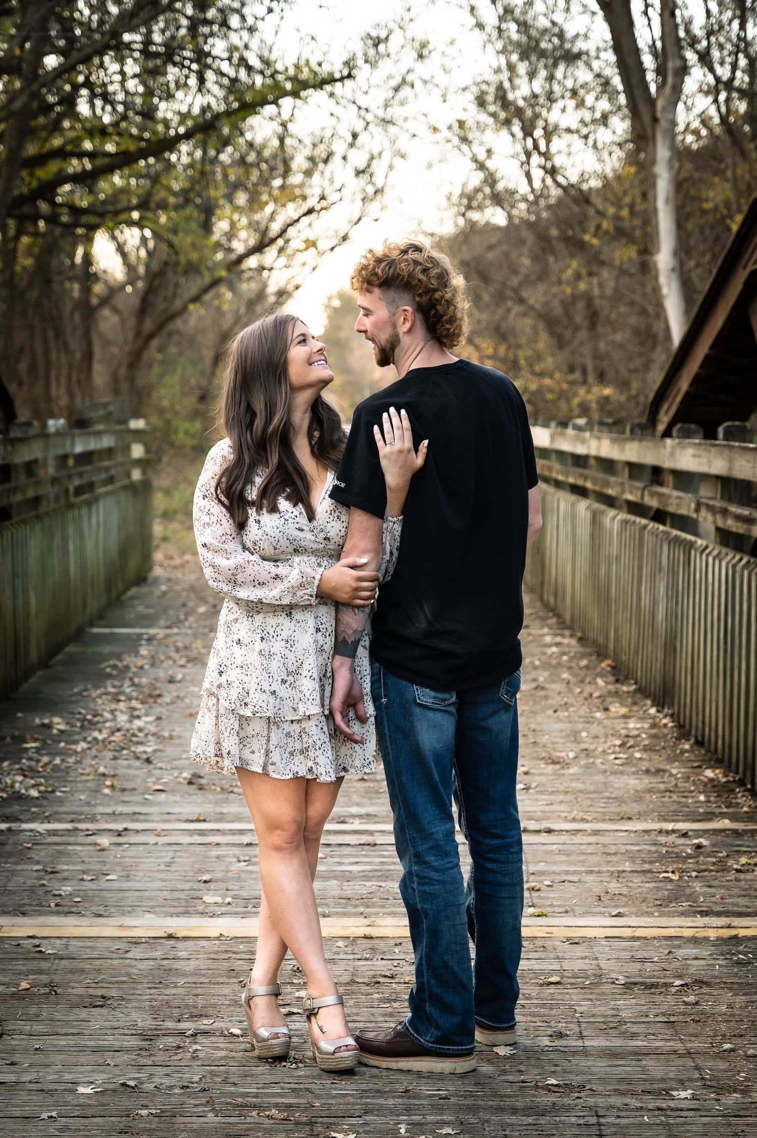 Couple walking together on a wooden boardwalk path during autumn with fallen leaves.